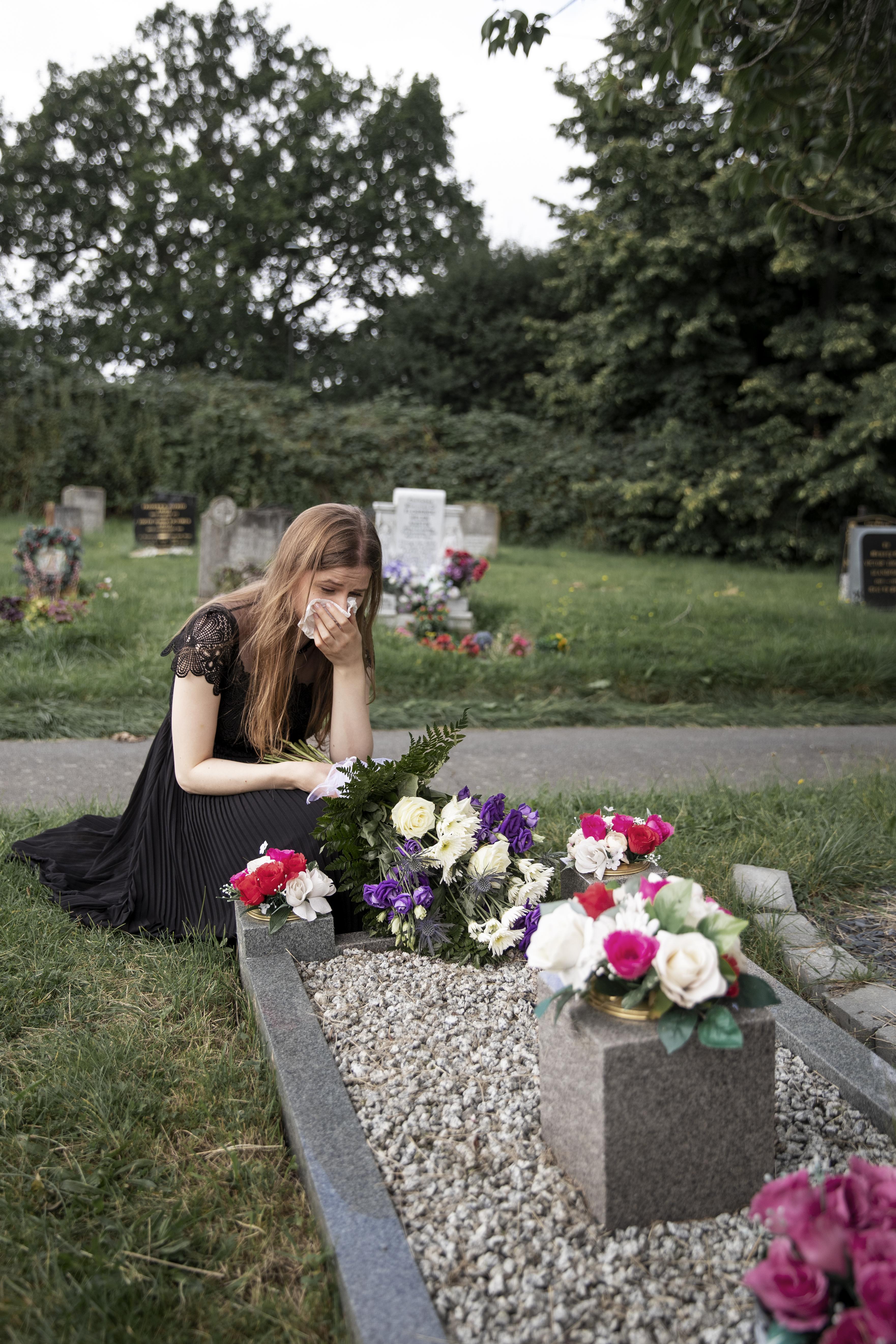 Une jeune femme en deuil devant une tombe dans un cimetière | Source : Freepik