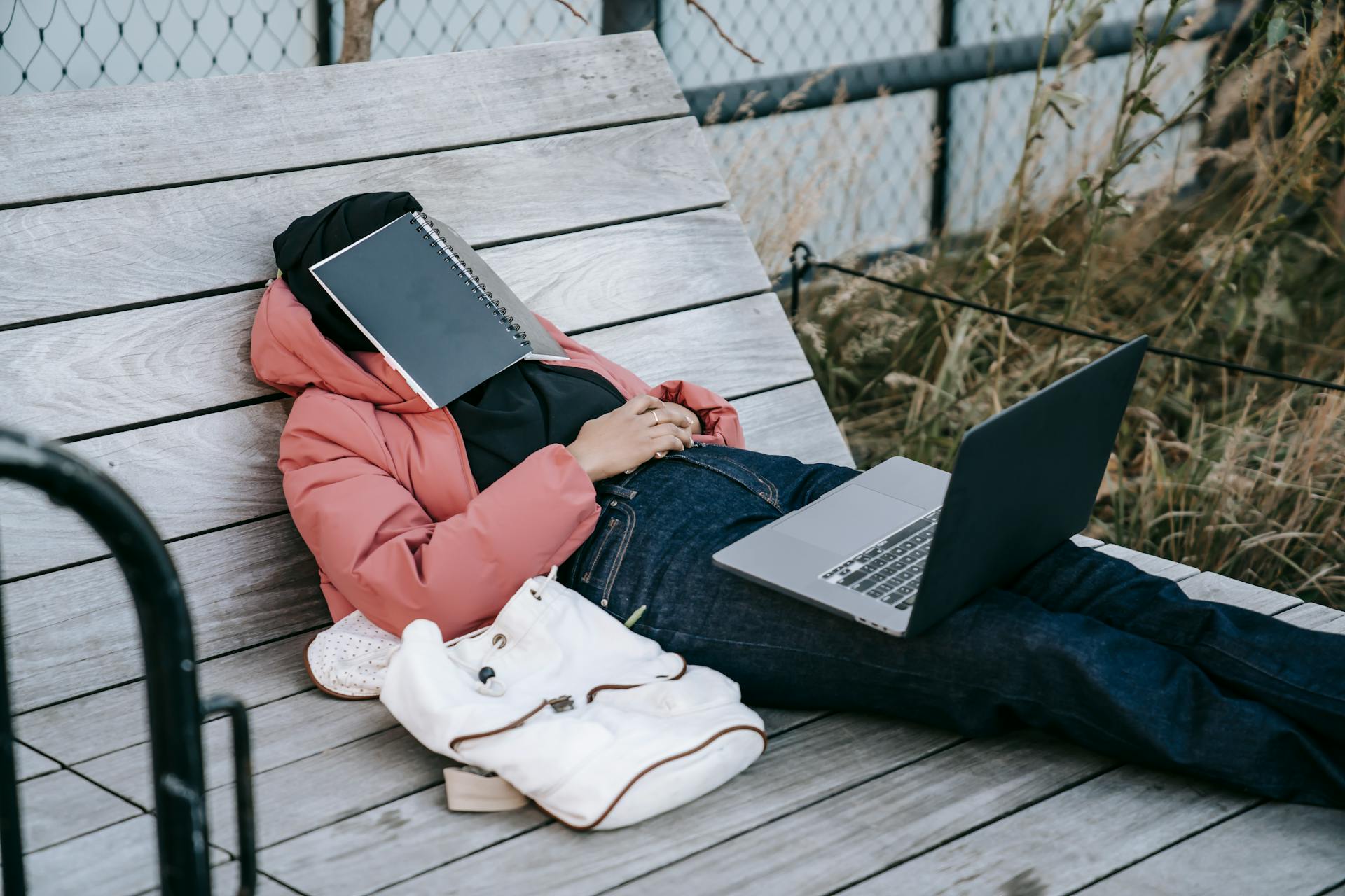 Une femme méconnaissable avec un ordinateur portable ouvert reposant sur un banc avec un livre sur le visage | Source : Pexels