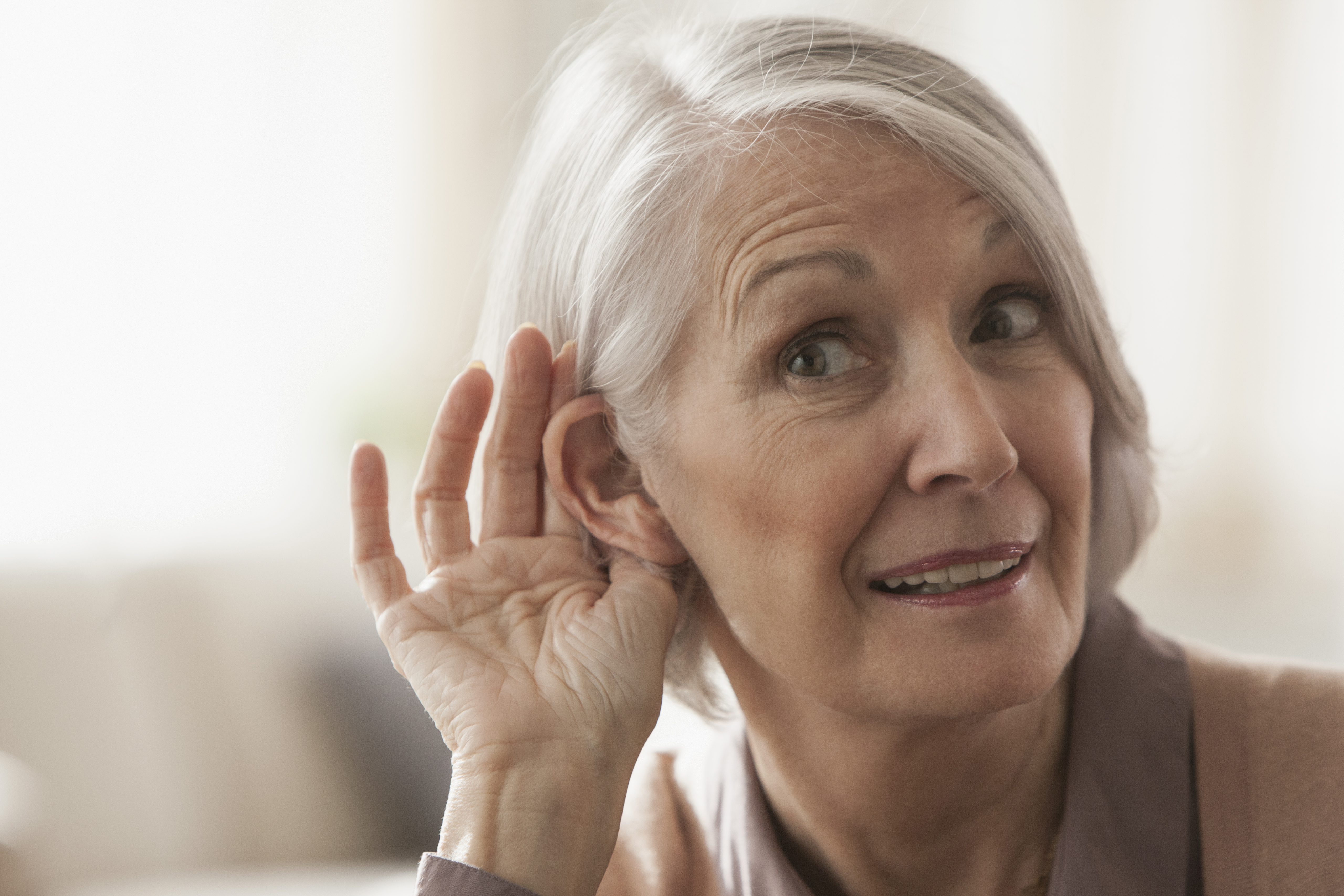 Une femme caucasienne âgée se met l'oreille en coupe pour écouter | Source : Getty Images