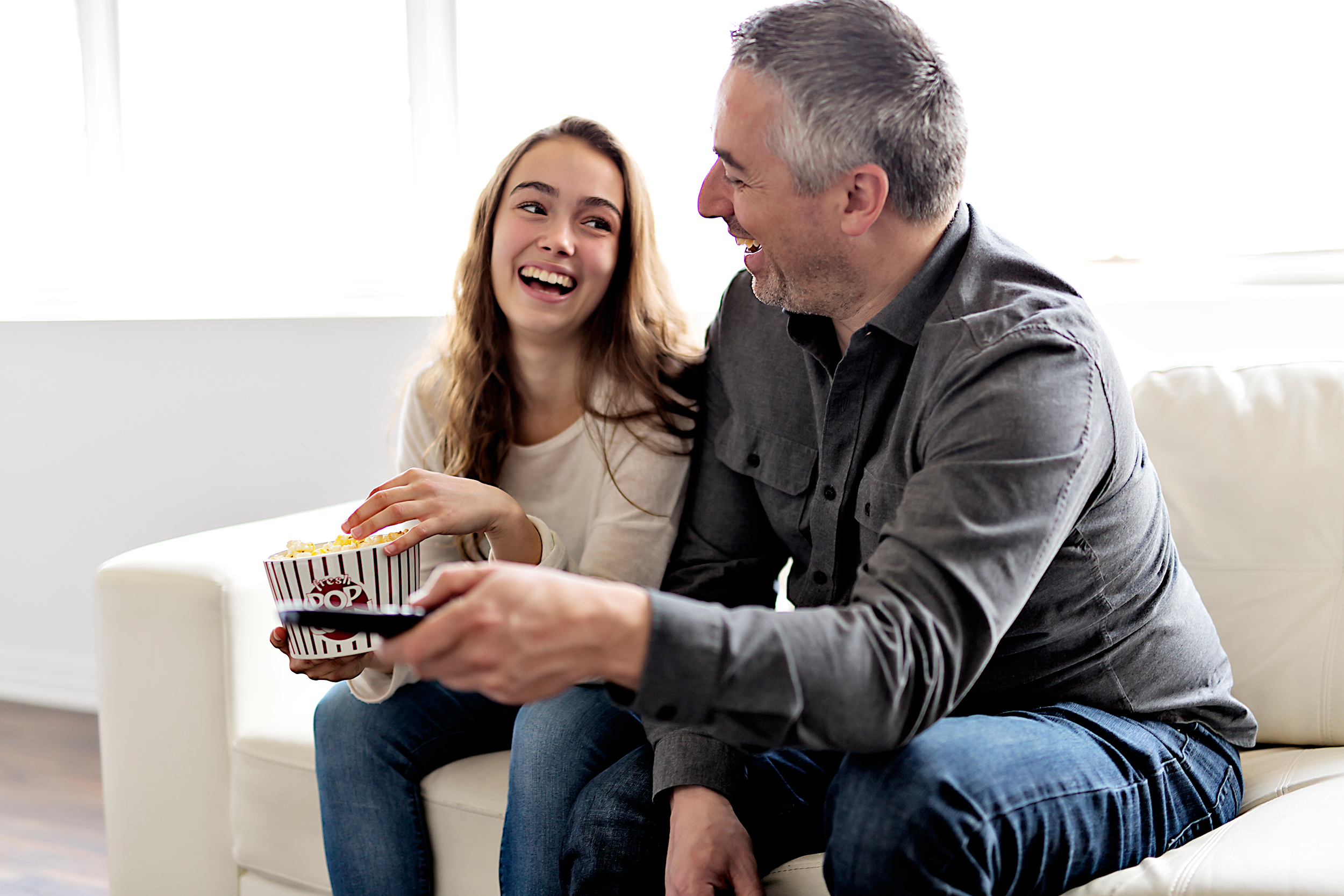Un duo papa-fille est photographié en train de rire ensemble en regardant la télévision et en mangeant du pop-corn | Source : Shutterstock