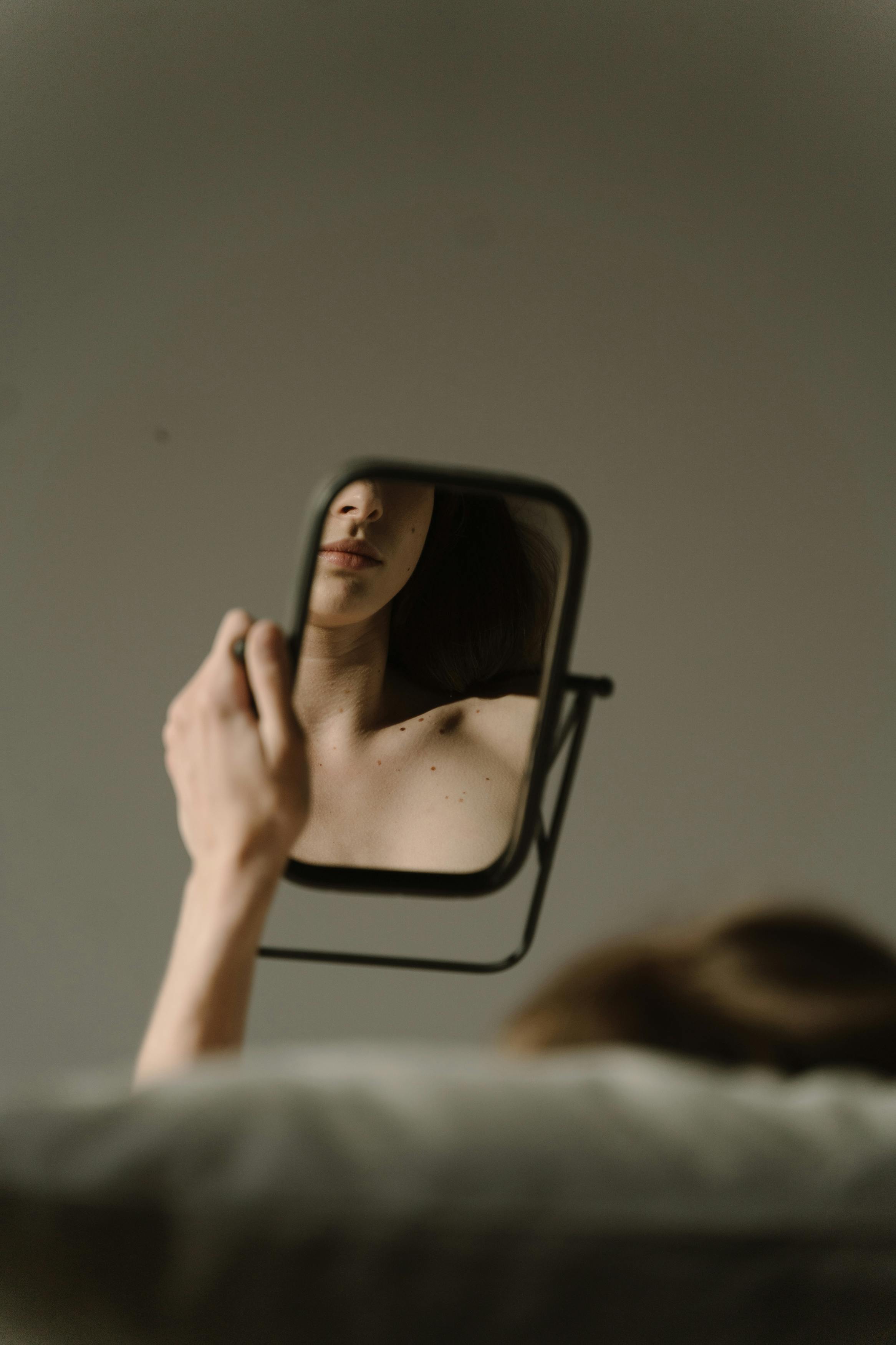 Une femme assise sur un canapé regardant son reflet sur un miroir | Source : Pexels
