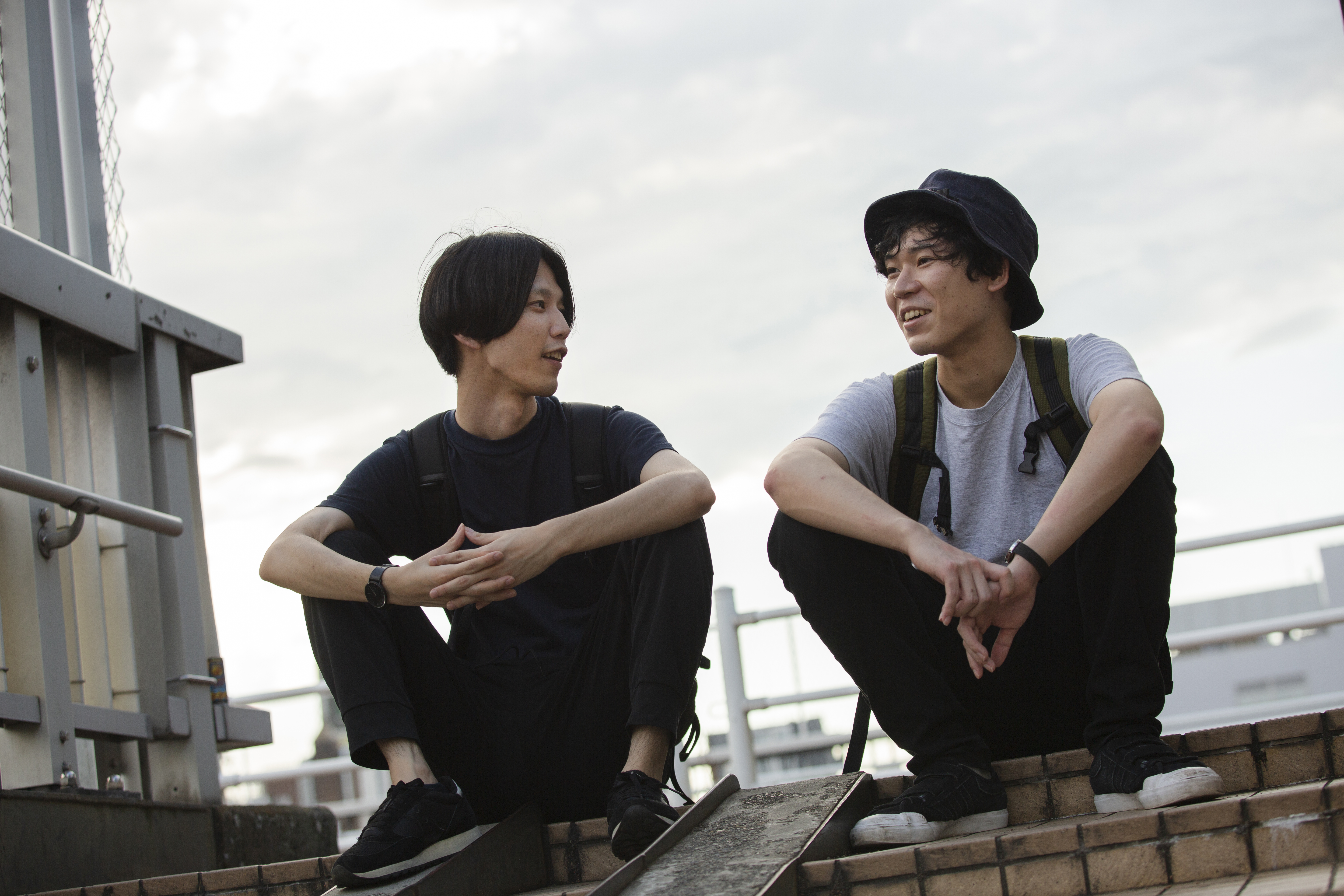 Deux jeunes hommes asiatiques assis sur un toit, en train de parler | Source : Getty Images