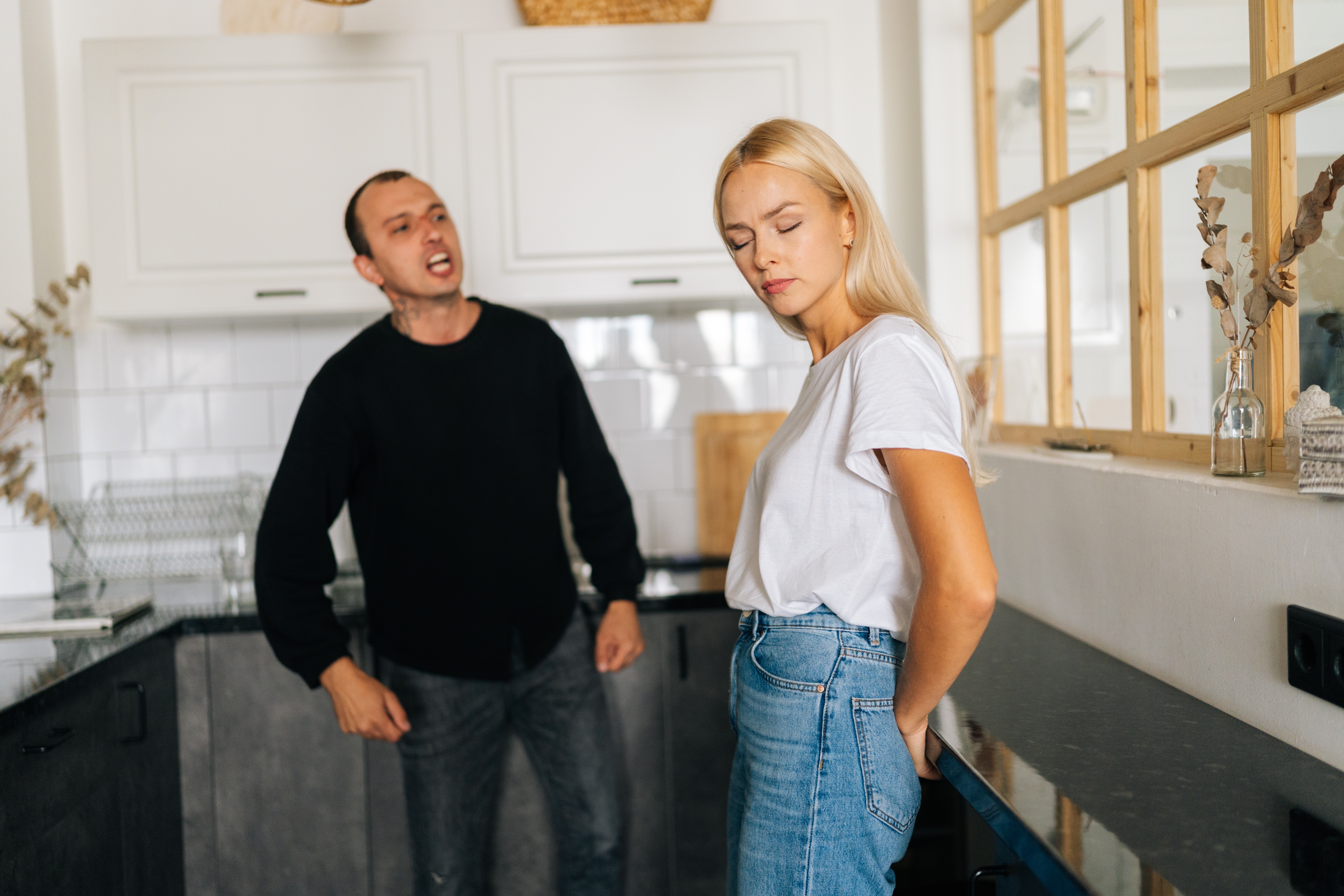 Une femme se tient dans la cuisine, les yeux fermés, alors que son homme lui crie dessus | Source : Shutterstock