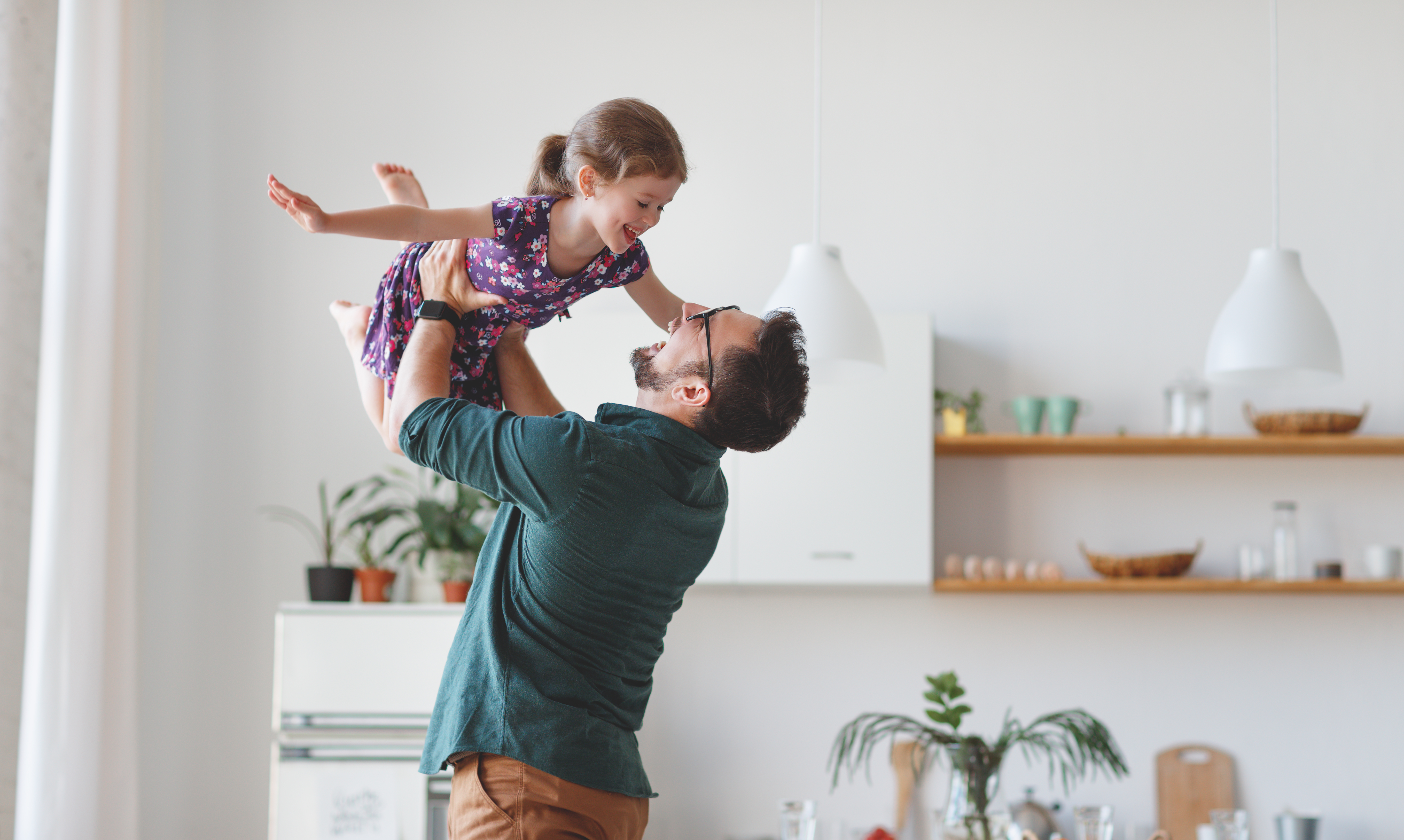 Un homme tenant sa fille au-dessus de sa tête alors qu'il lui sourit | Source : Shutterstock