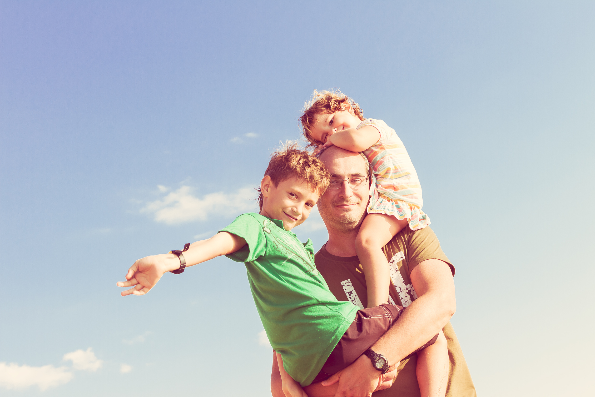 Un père tenant son fils dans ses bras et sa fille sur ses épaules | Source : Shutterstock