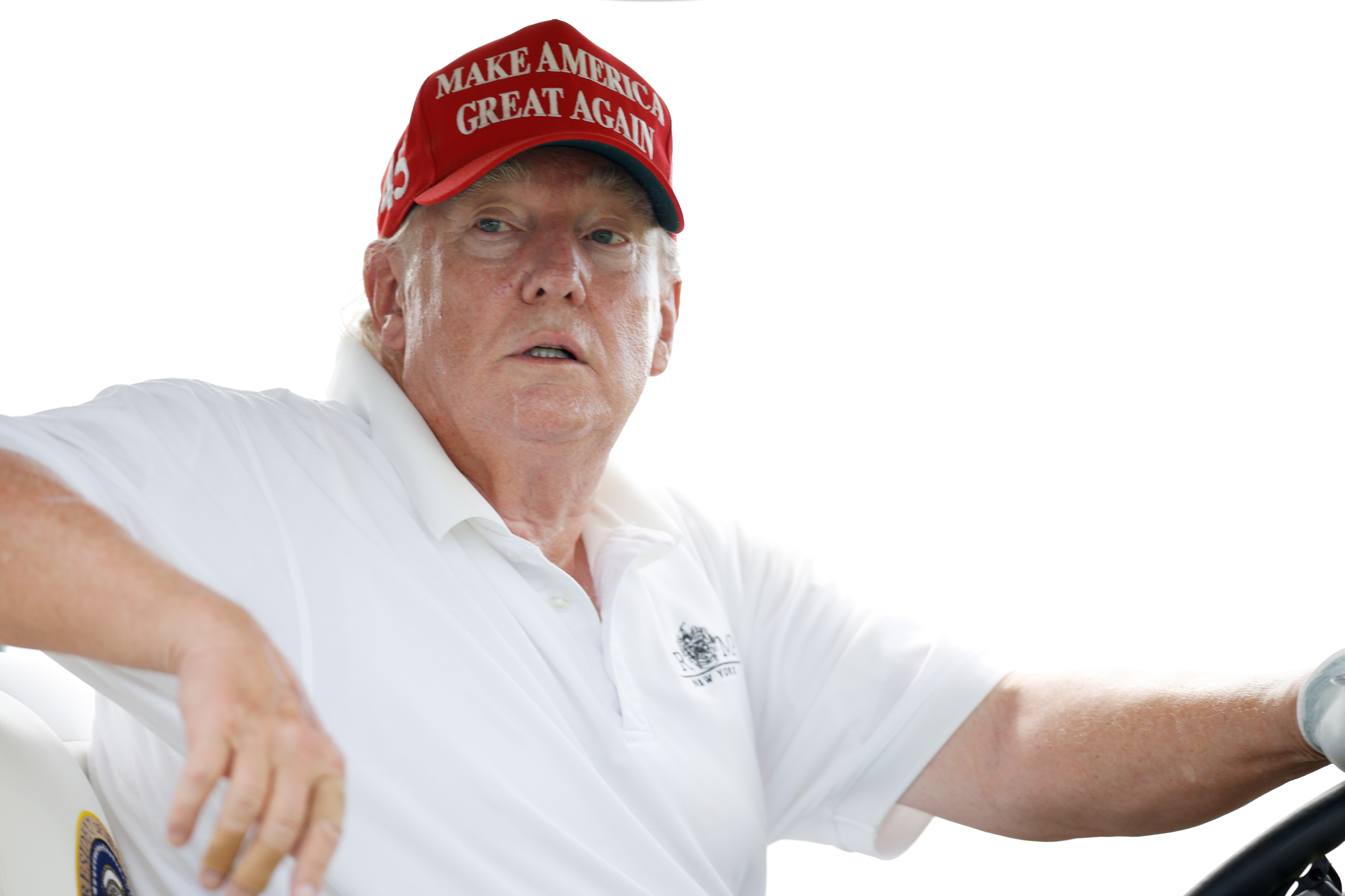 En gros plan, alors qu'il conduit le chariot, la peau de Donald Trump apparaît rougie autour des joues et des yeux, avec des zones plus pâles près de ses oreilles et de son col. Son polo reste ouvert au niveau du cou, révélant davantage de contraste dans les tons.