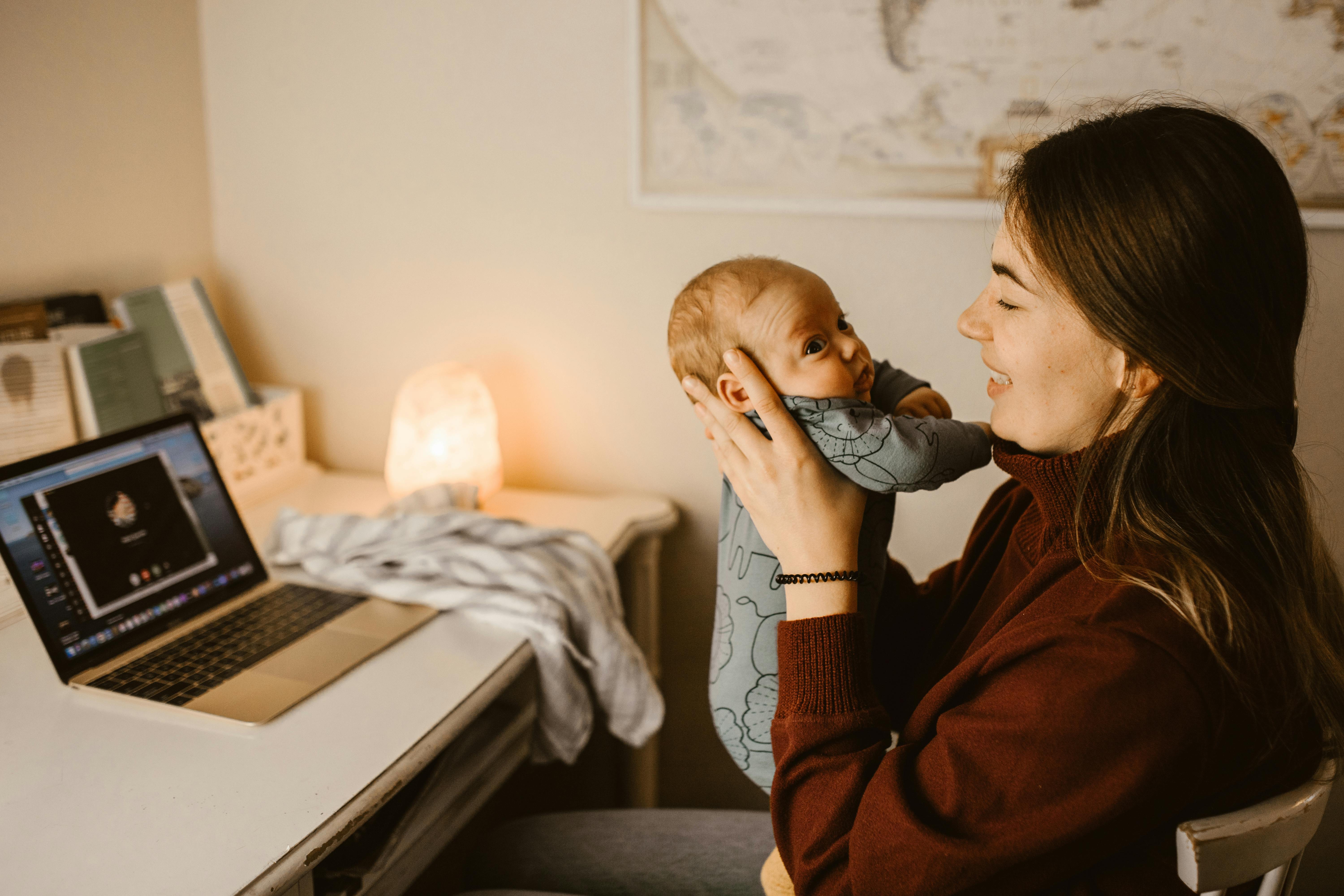 Une femme tenant son bébé alors qu'elle est assise à son bureau | Source : Pexels