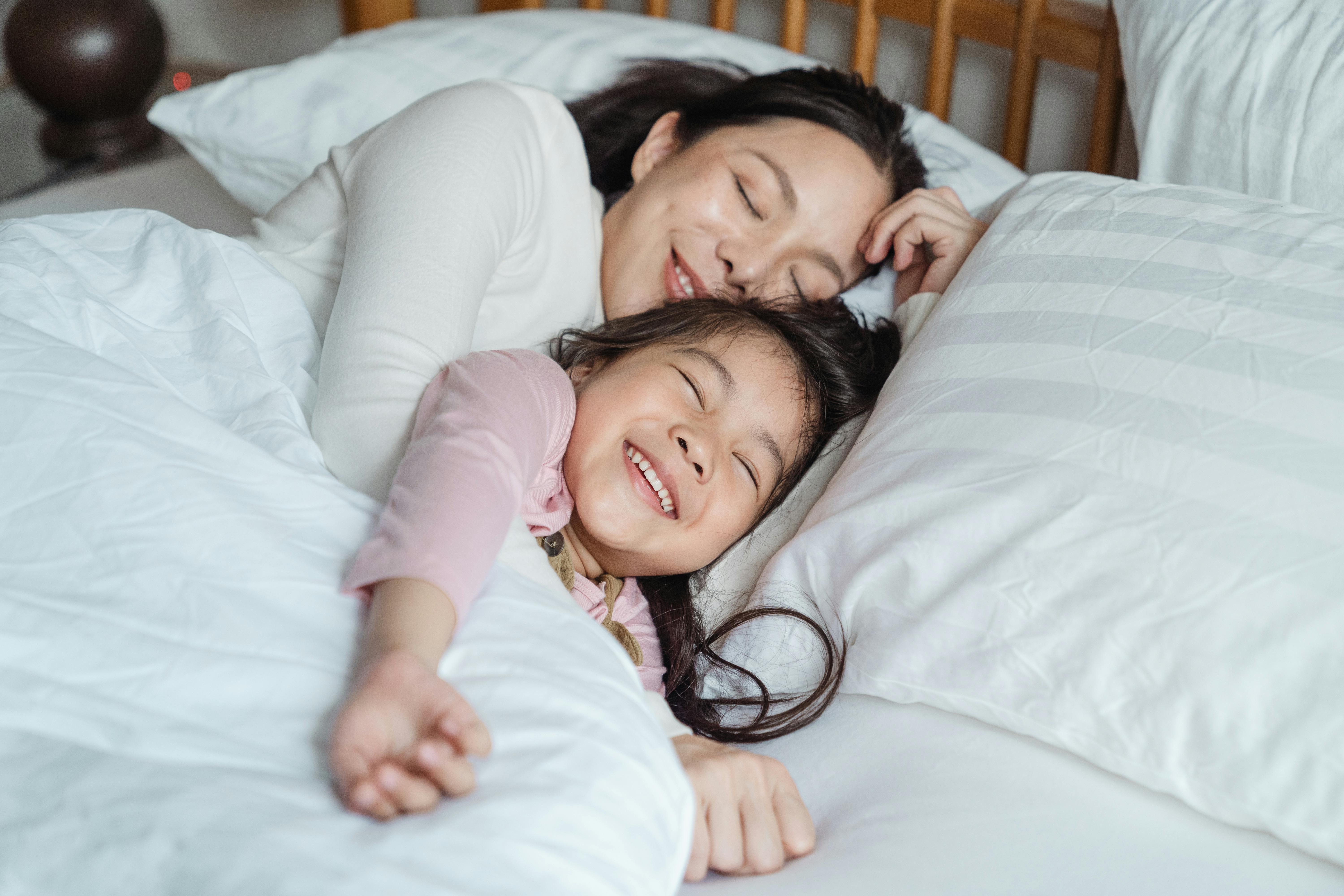 Une femme sourit tout en réconfortant une petite fille alors qu'elles sont allongées dans un lit ensemble | Source : Pexels