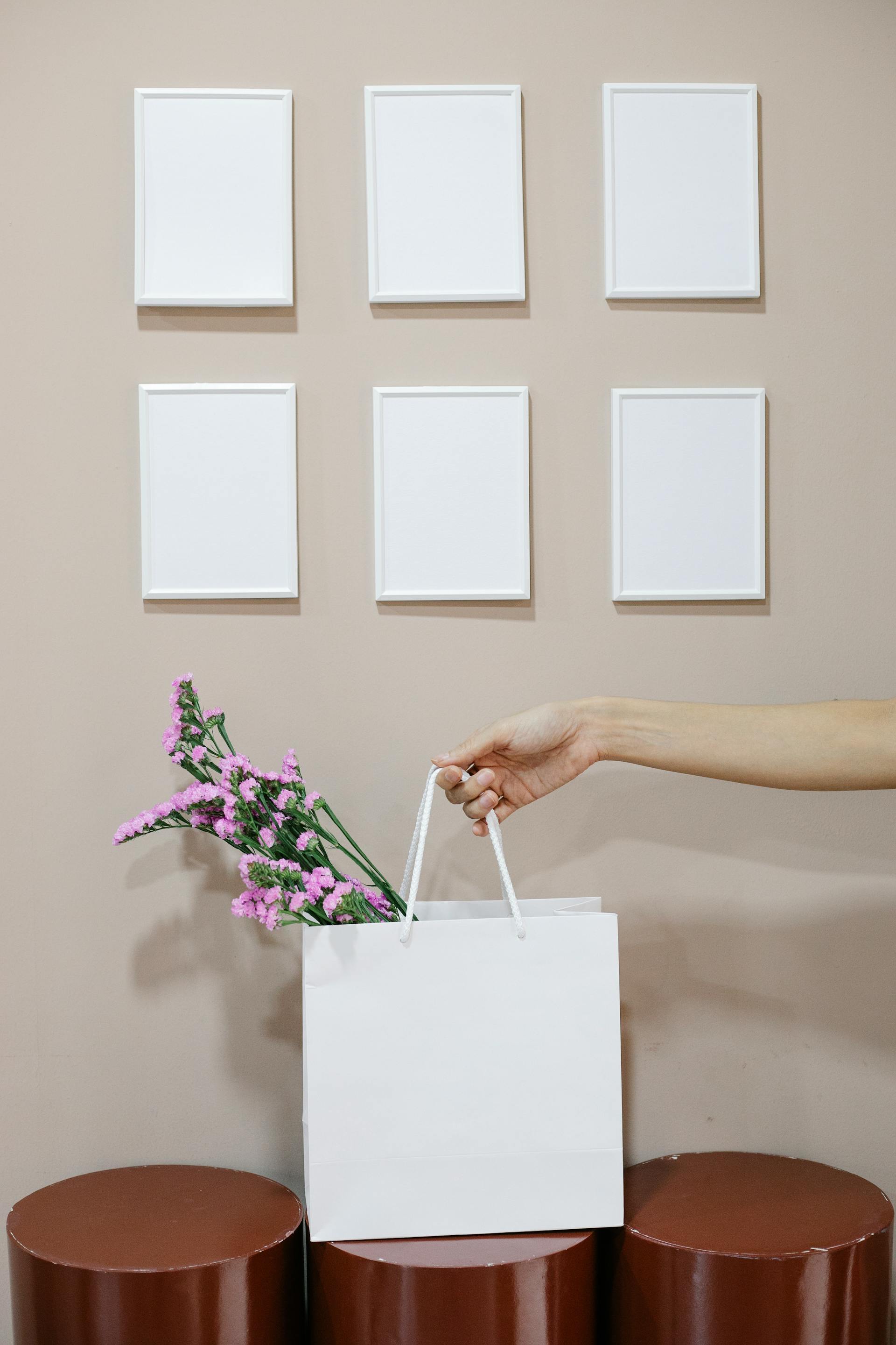 Photo en gros plan d'une femme tenant un sac en papier avec des fleurs près d'un mur avec des cadres vierges | Source : Pexels