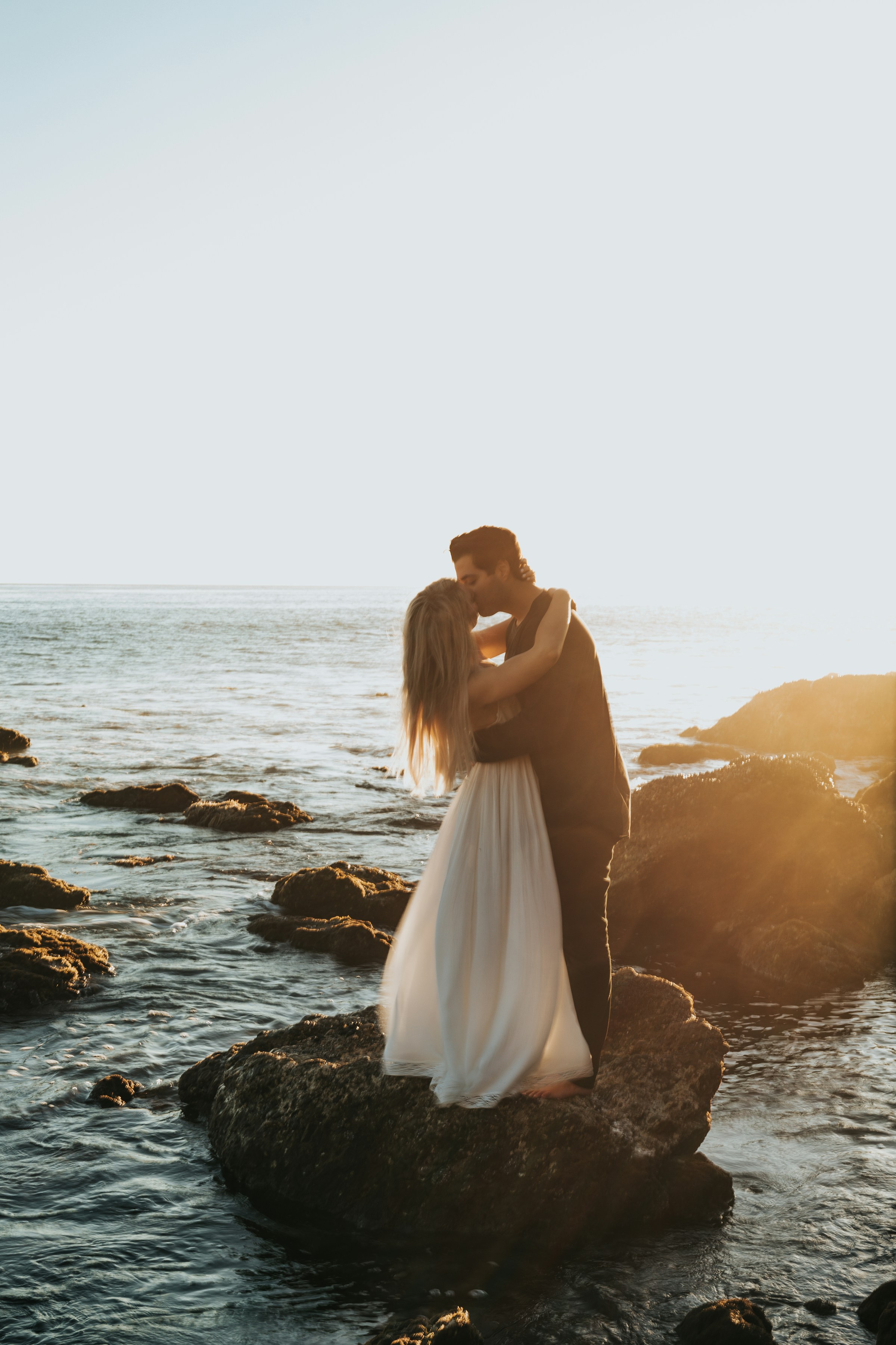 Un couple s'embrasse en se tenant au sommet d'un rocher sur une plage | Source : Unsplash