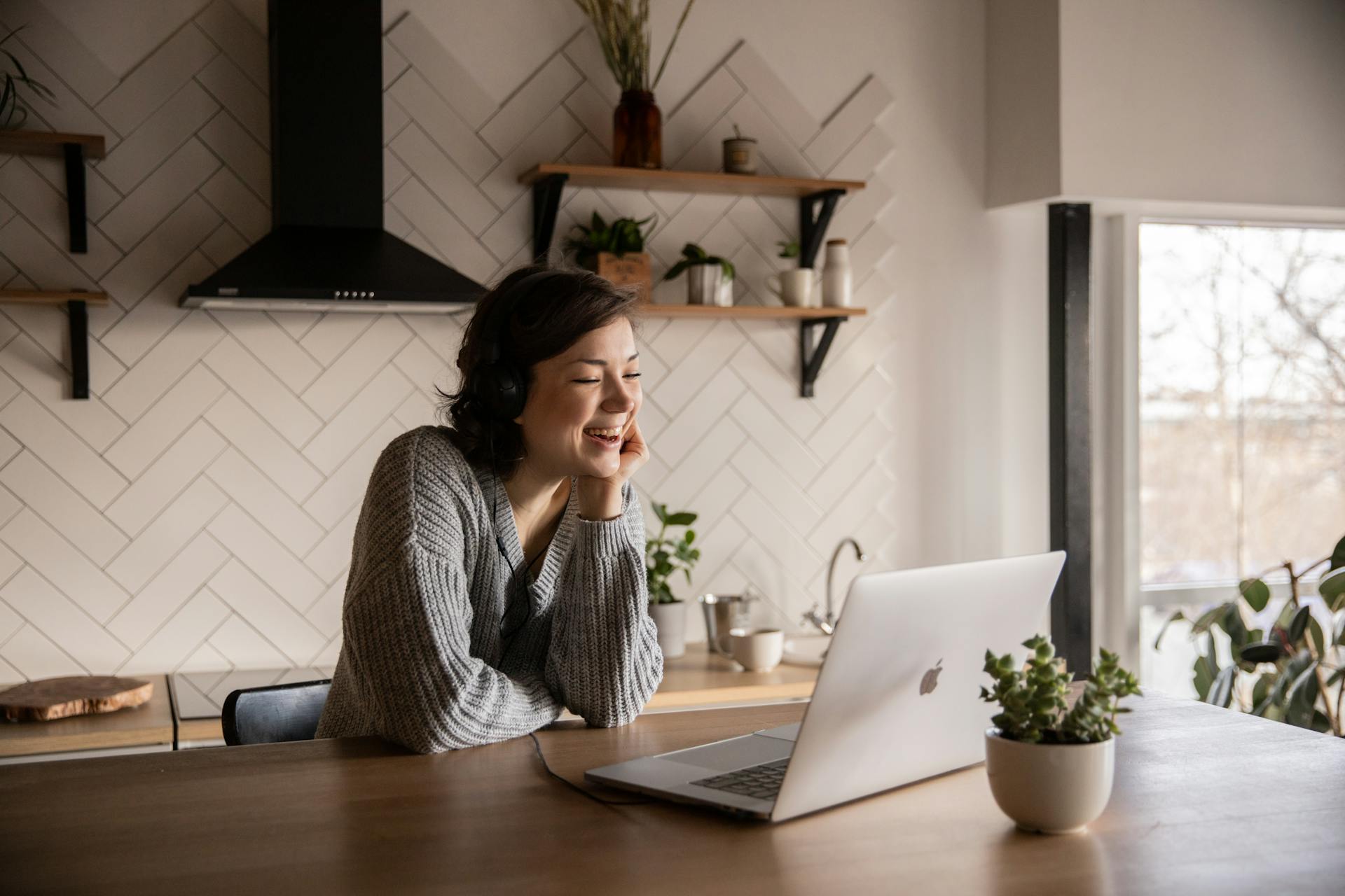 Une femme souriante parle via un ordinateur portable alors qu'elle est assise dans la cuisine | Source : Pexels