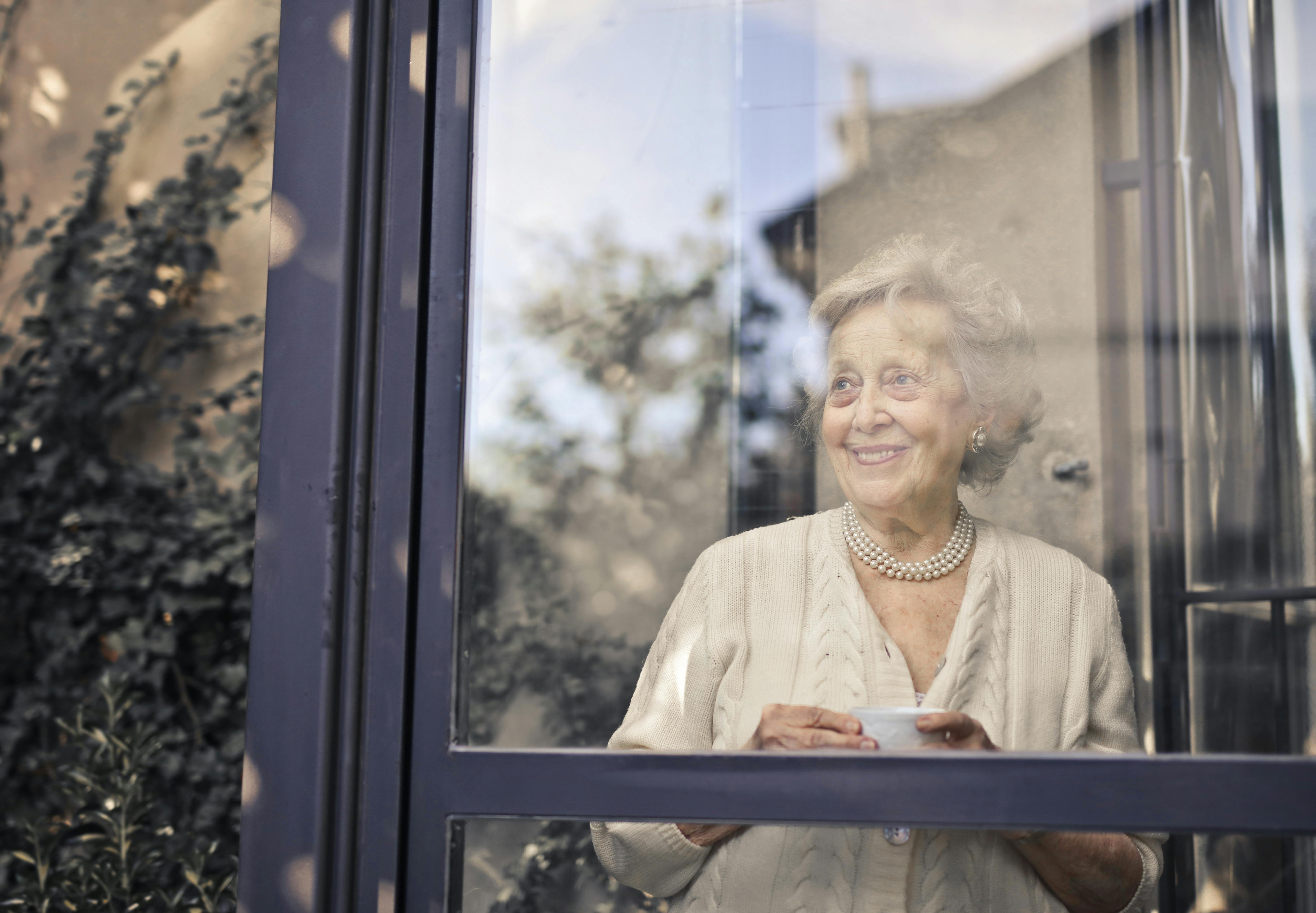 Une femme âgée souriante qui regarde par sa fenêtre | Source : Pexels