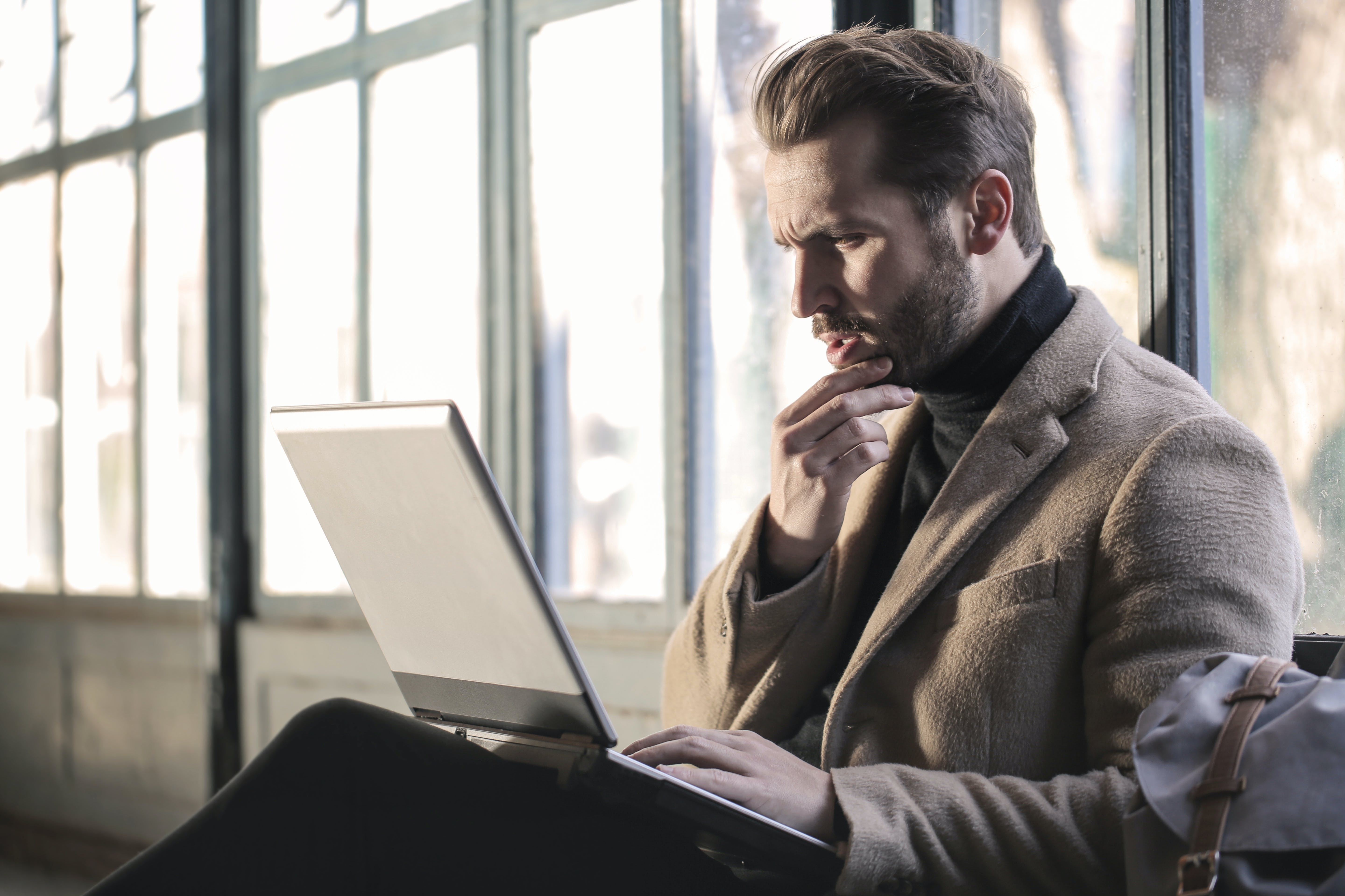 Un homme confus se tenant le menton alors qu'il est assis en train de regarder un ordinateur portable | Source : Pexels