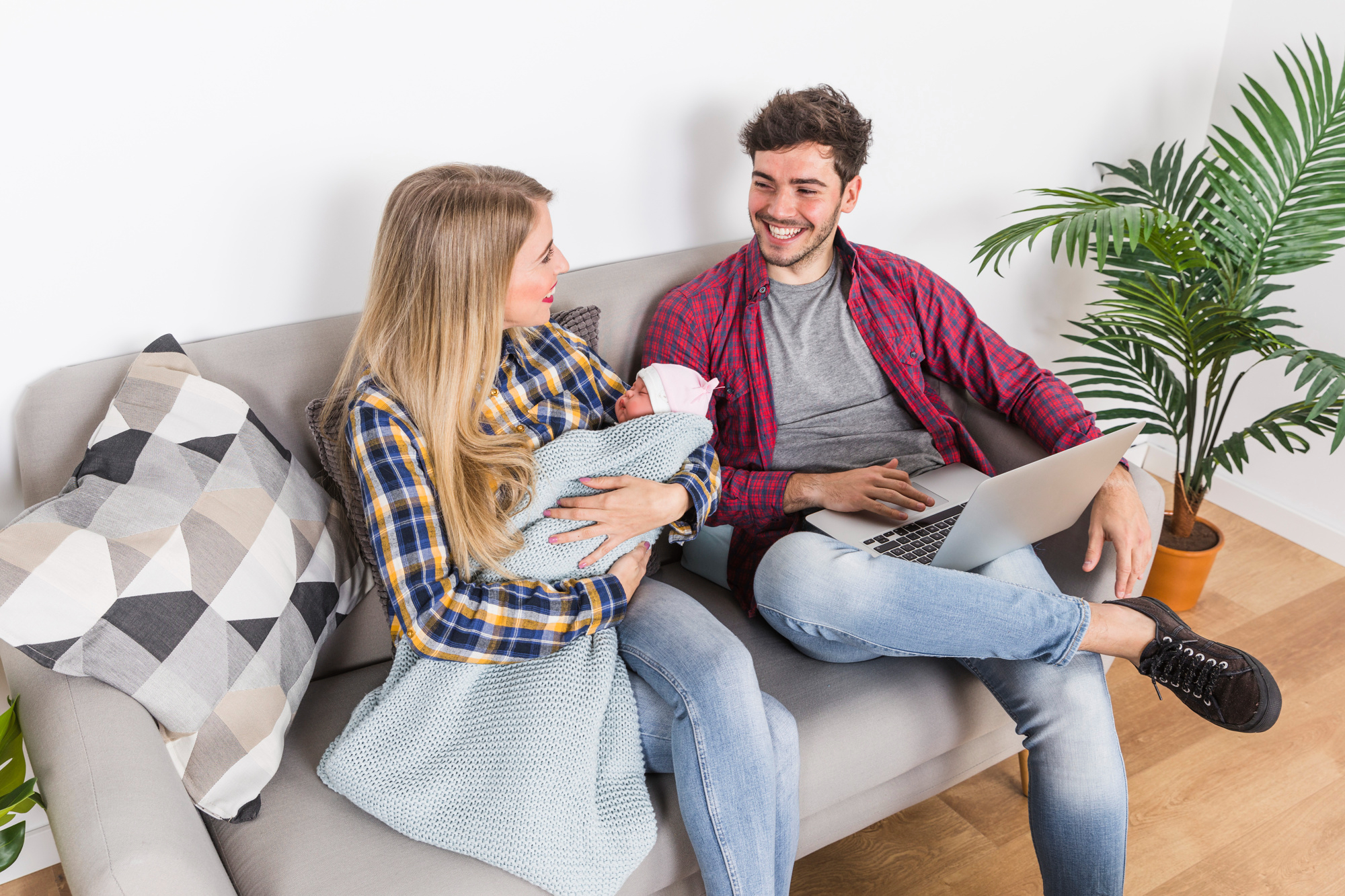 Une femme avec un bébé regarde son mari qui utilise un ordinateur portable | Source : Freepik