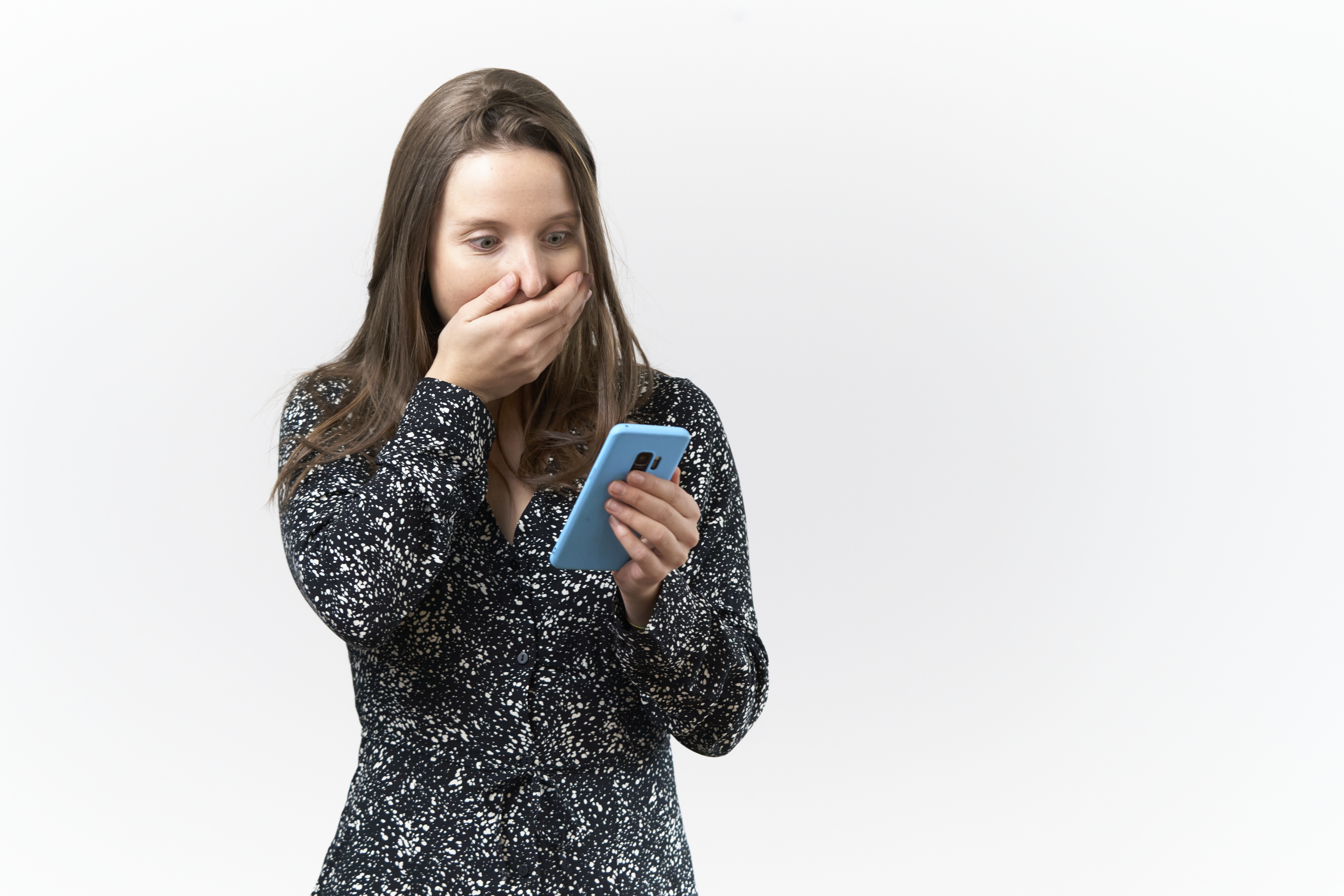 Jeune femme à l'expression surprise lisant des messages sur son téléphone portable sur fond blanc | Source : Getty Images