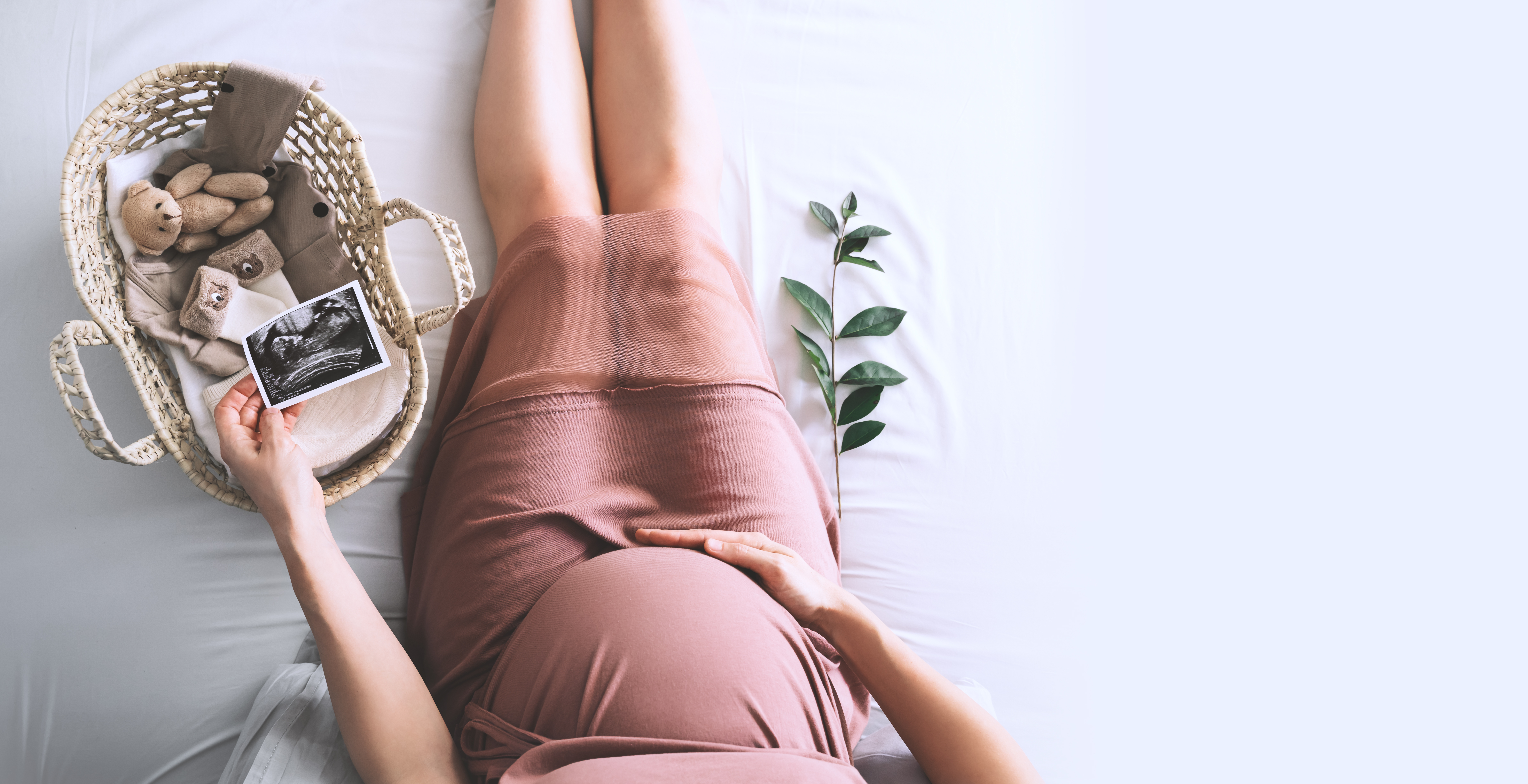 Une femme tenant la photo de l'échographie de son bébé dans une main et son ventre de femme enceinte dans l'autre, à côté d'un panier de fournitures pour bébé | Source : Shutterstock