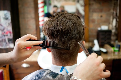 Vue arrière d'un jeune homme chez le coiffeur en train de se faire couper les cheveux. | Photo : Getty Images