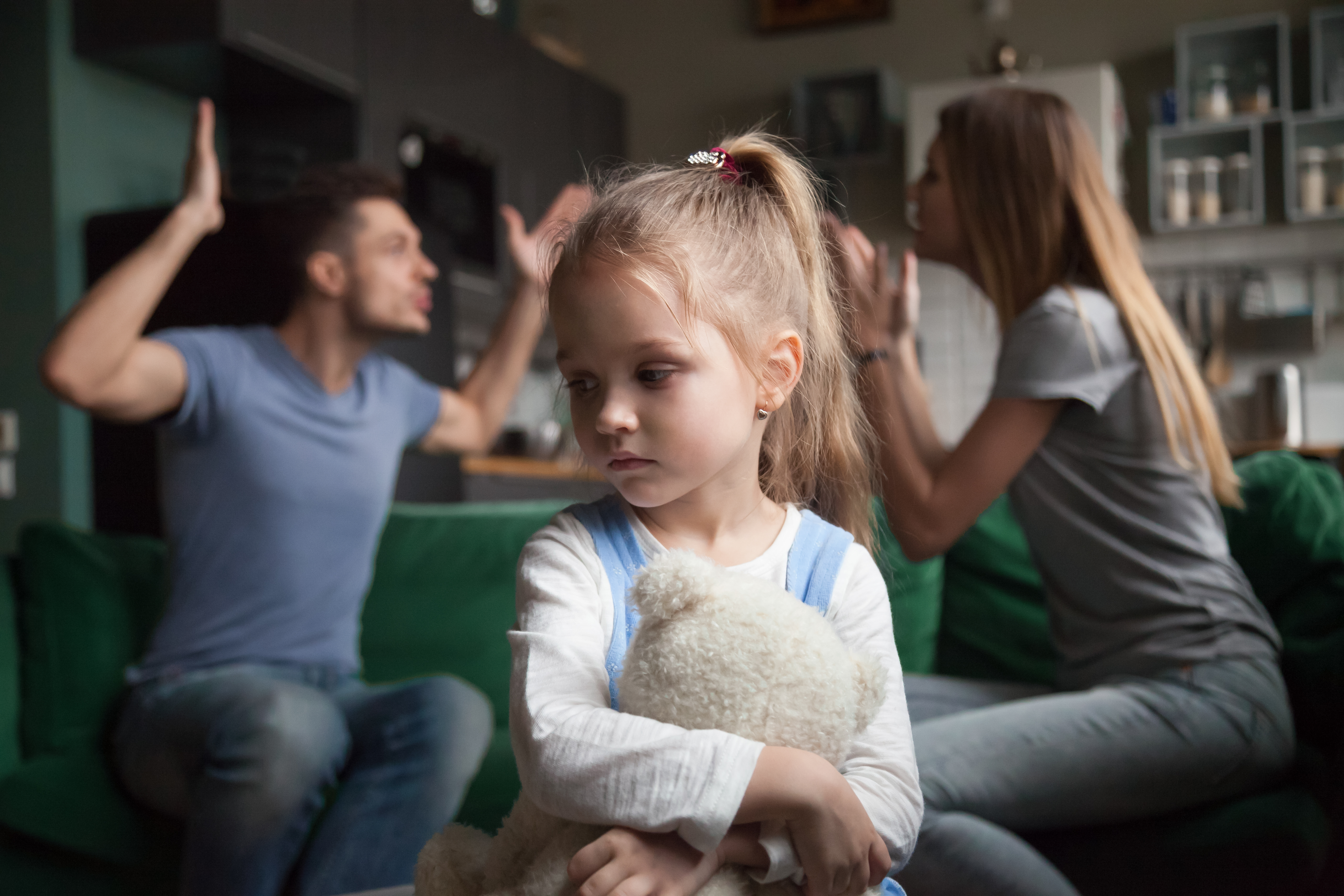 Une petite fille qui se sent contrariée tandis que ses parents se disputent en arrière-plan | Source : Shutterstock