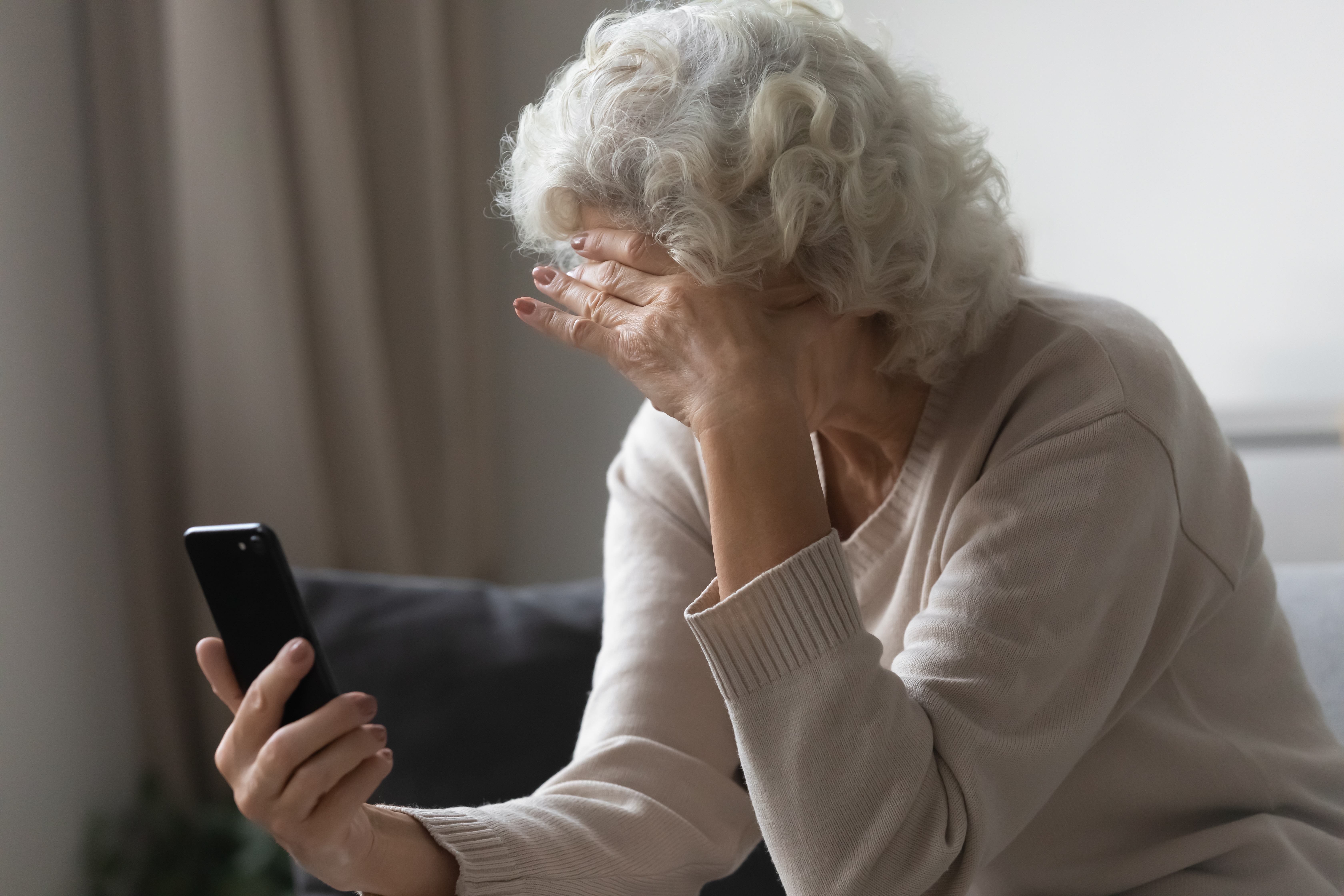 Une femme âgée a l'air préoccupée alors qu'elle tient un téléphone portable. Source : Shutterstock