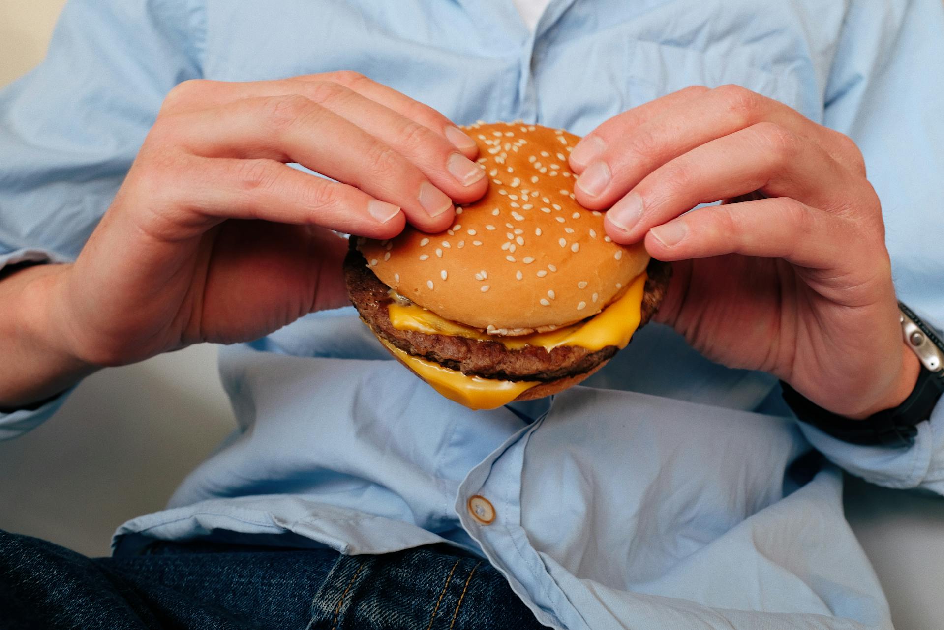Gros plan recadré d'un homme tenant un hamburger | Source : Pexels