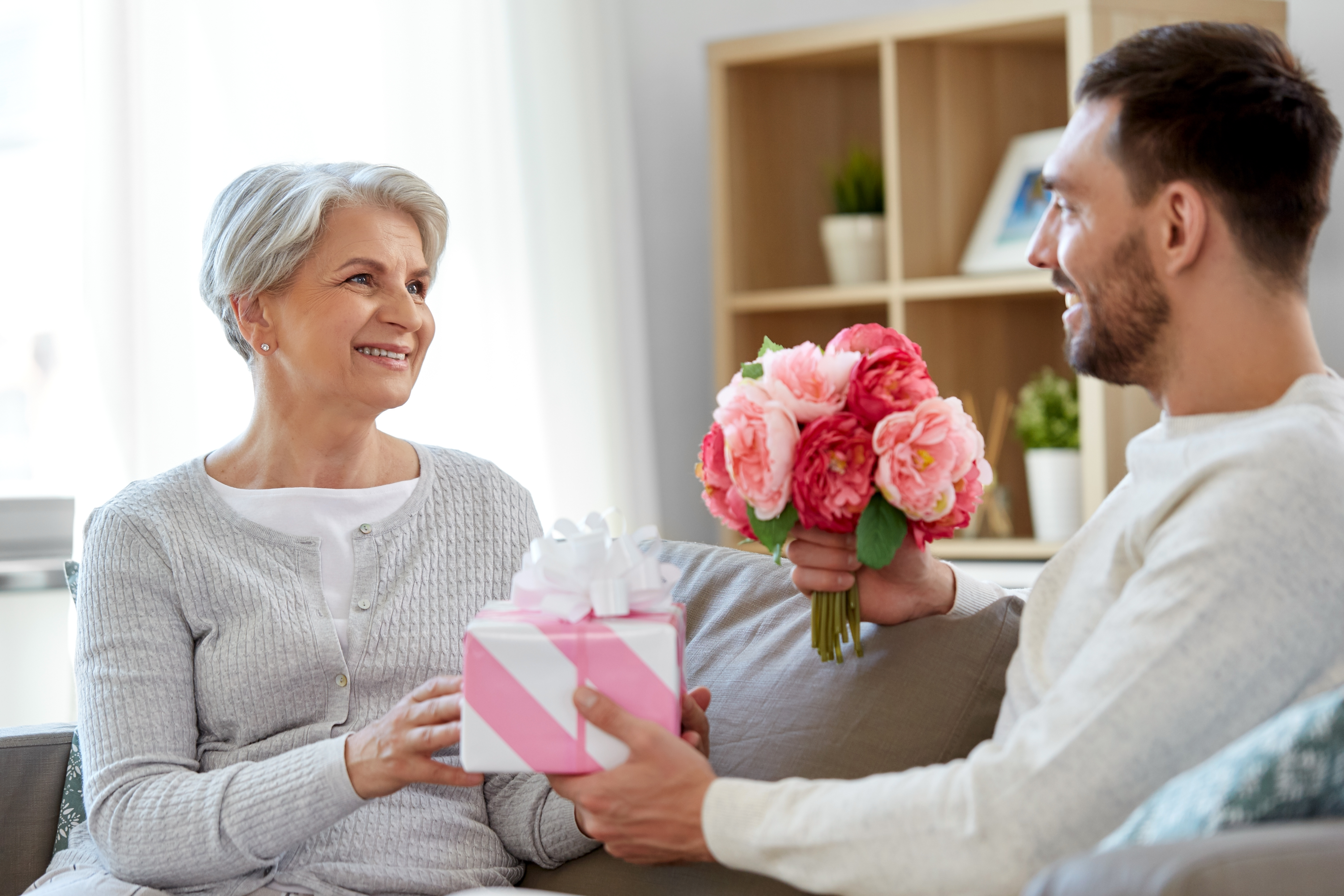 Un fils adulte offrant un cadeau et des fleurs à sa mère âgée | Source : Shutterstock