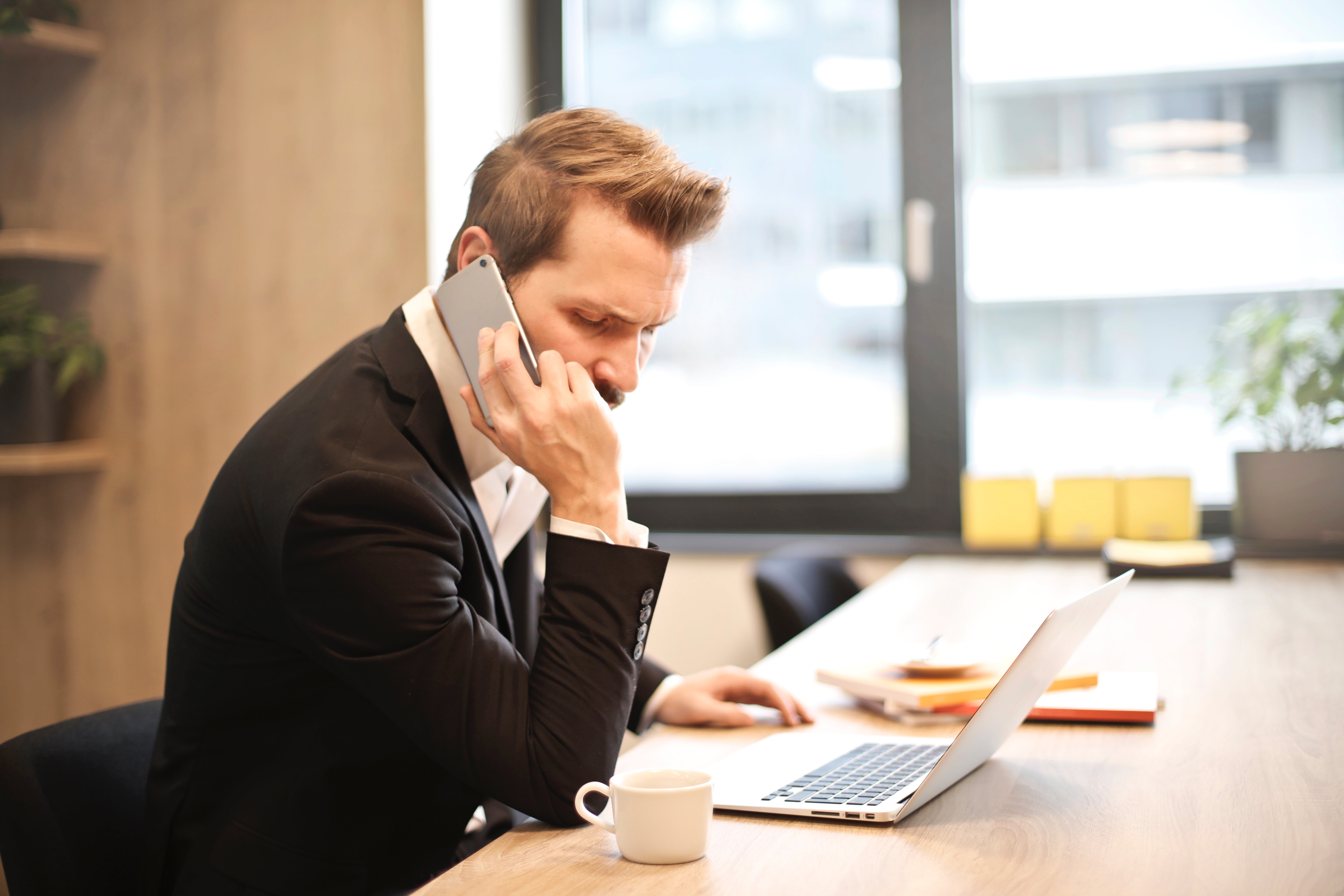 Un homme assis à un bureau avec un ordinateur portable tout en ayant l'air mécontent pendant un appel | Source : Pexels