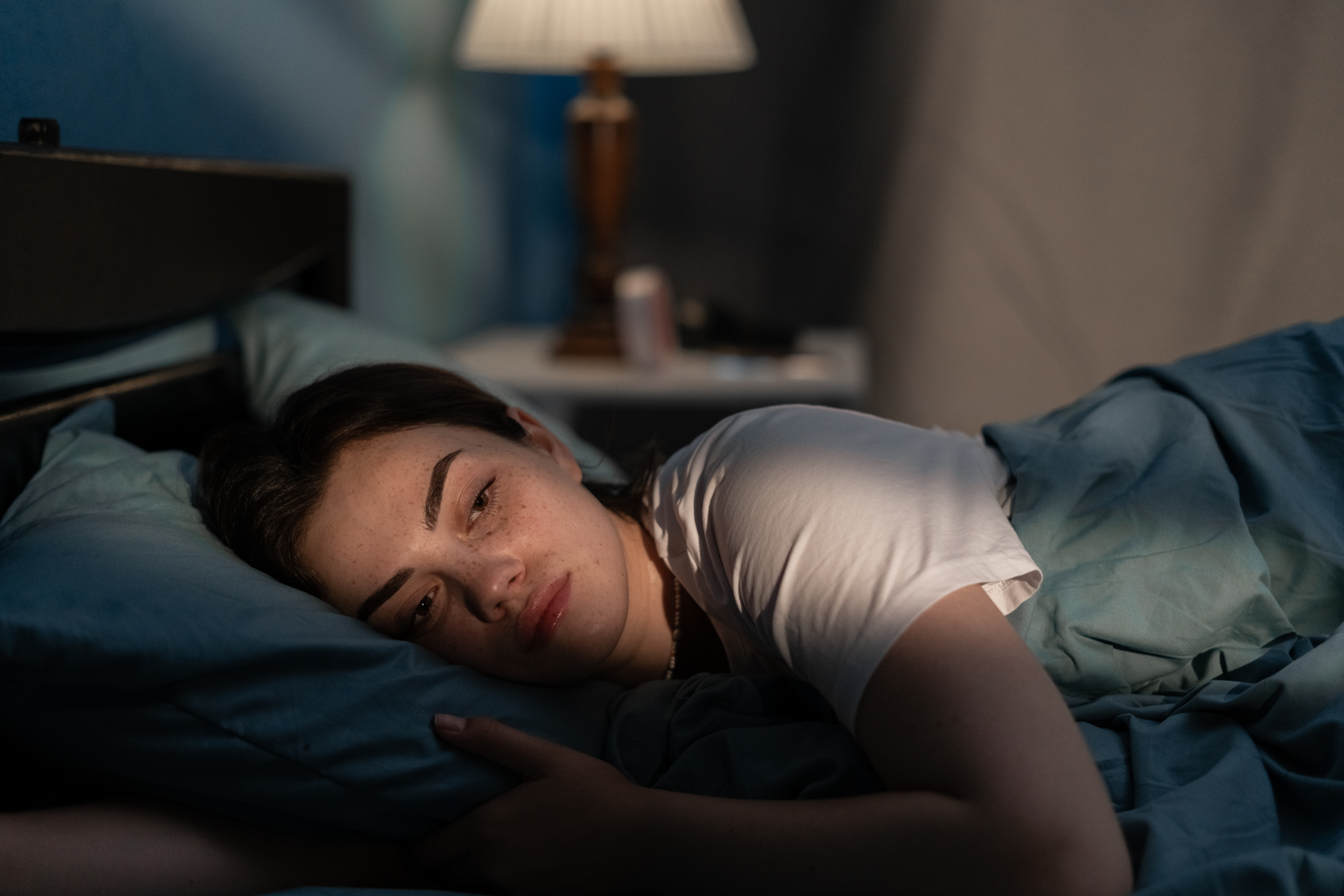 Jeune femme triste allongée dans son lit tard dans la nuit essayant de dormir souffrant d'insomnie. | Source : Getty Images