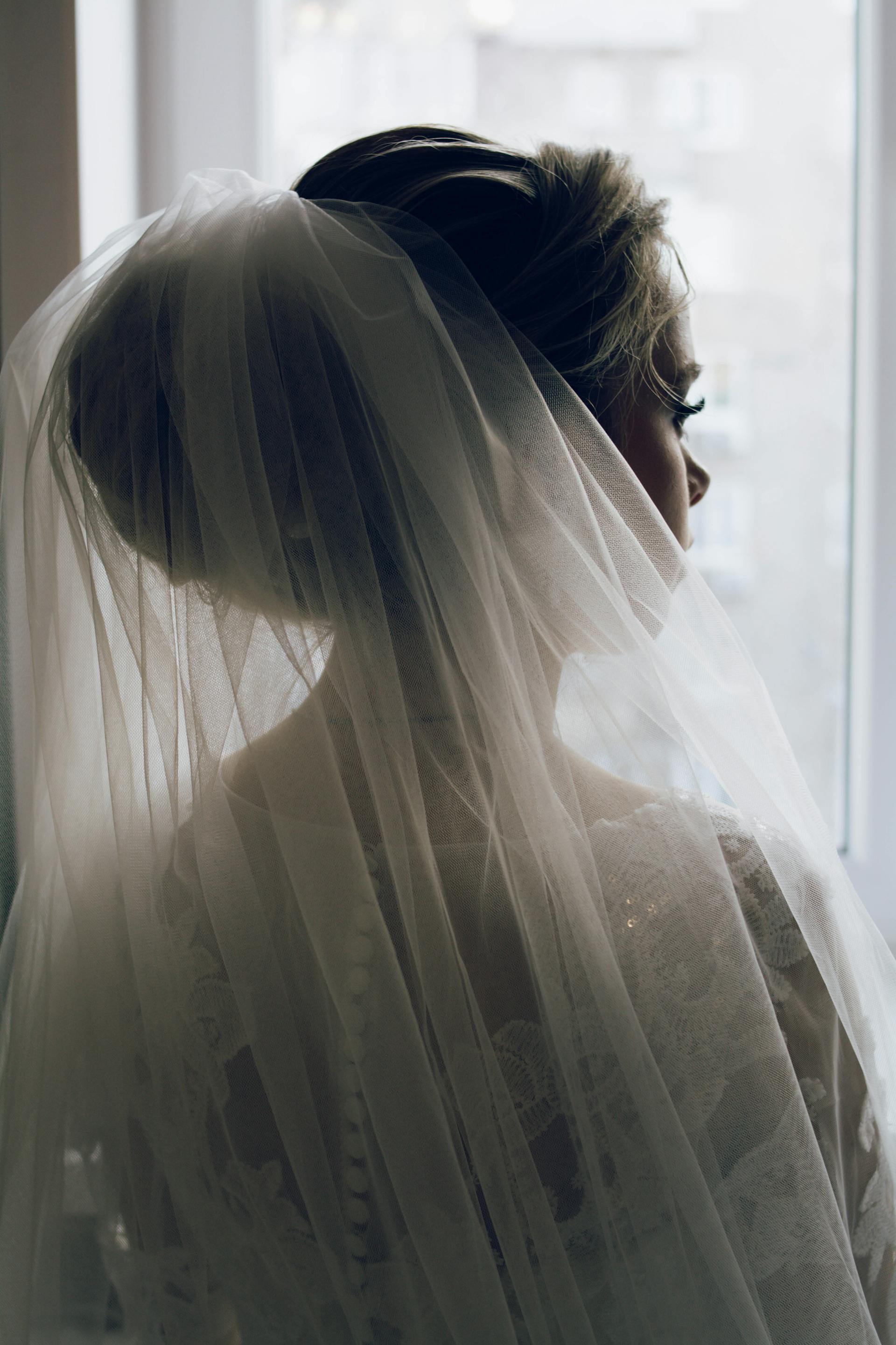 Une mariée en robe de mariée et voile regardant par la fenêtre | Source : Pexels