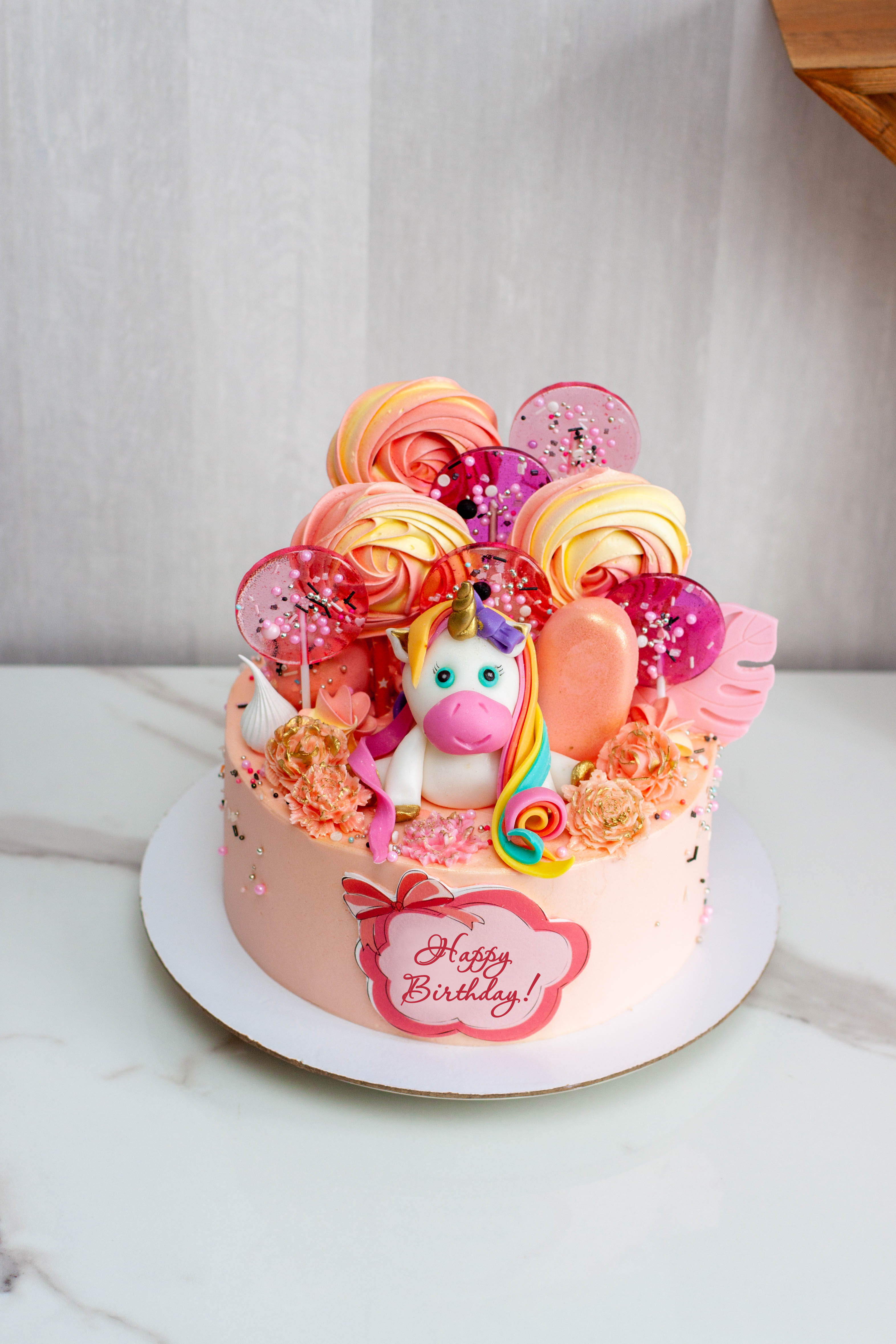 Gâteau d'anniversaire avec une jolie licorne en fondant, des lollipos, des meringues, des popsicles et des fleurs en chocolat pour une fille ou un bébé. Texte Joyeux anniversaire | Source : Getty Images