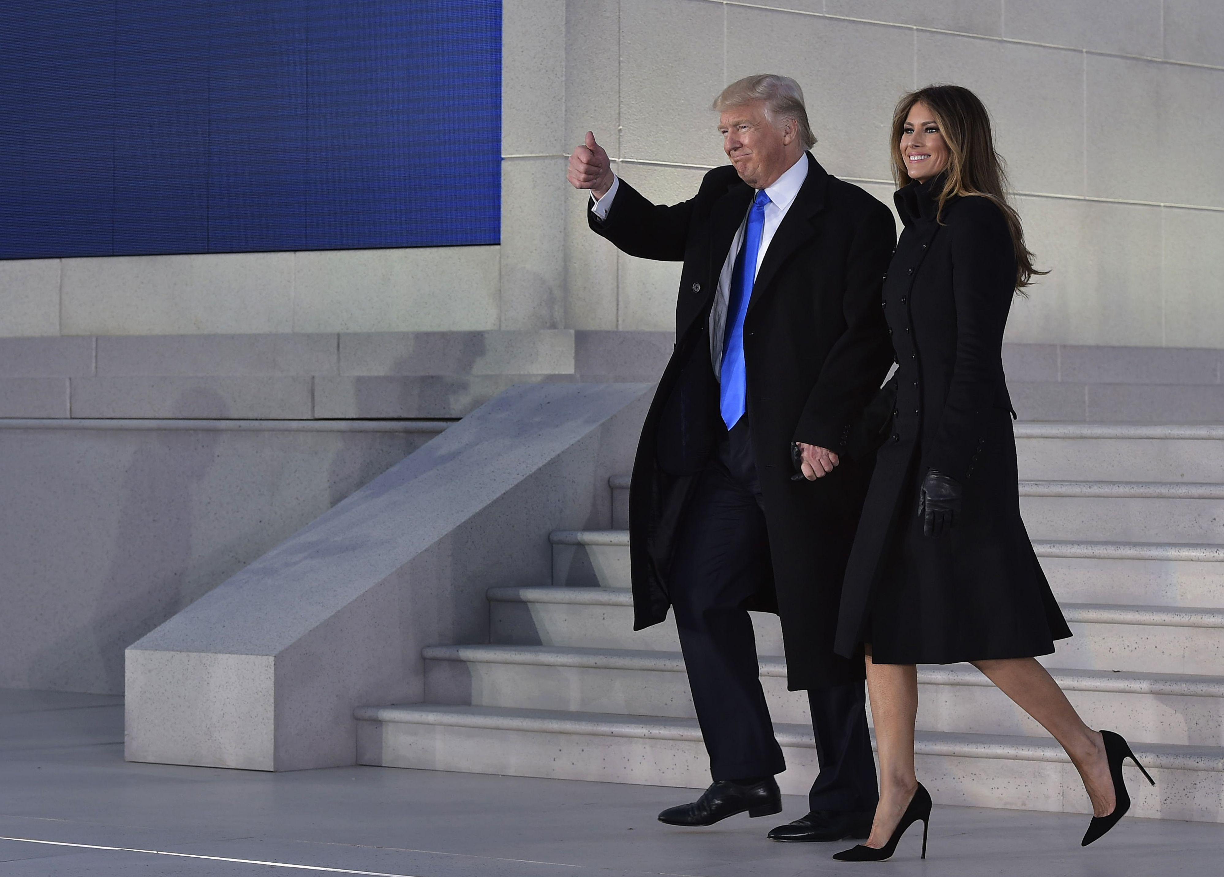 Melania Trump arrive à une cérémonie de bienvenue organisée avant l'investiture au Lincoln Memorial à Washington, D.C., le 19 janvier 2017. Elle porte une robe-manteau noire à double boutonnage d'inspiration militaire, avec des gants noirs, et des escarpins noirs à bout pointu et talon aiguille qui lui donnent une allure classique et très haute, sur les marches de pierre.