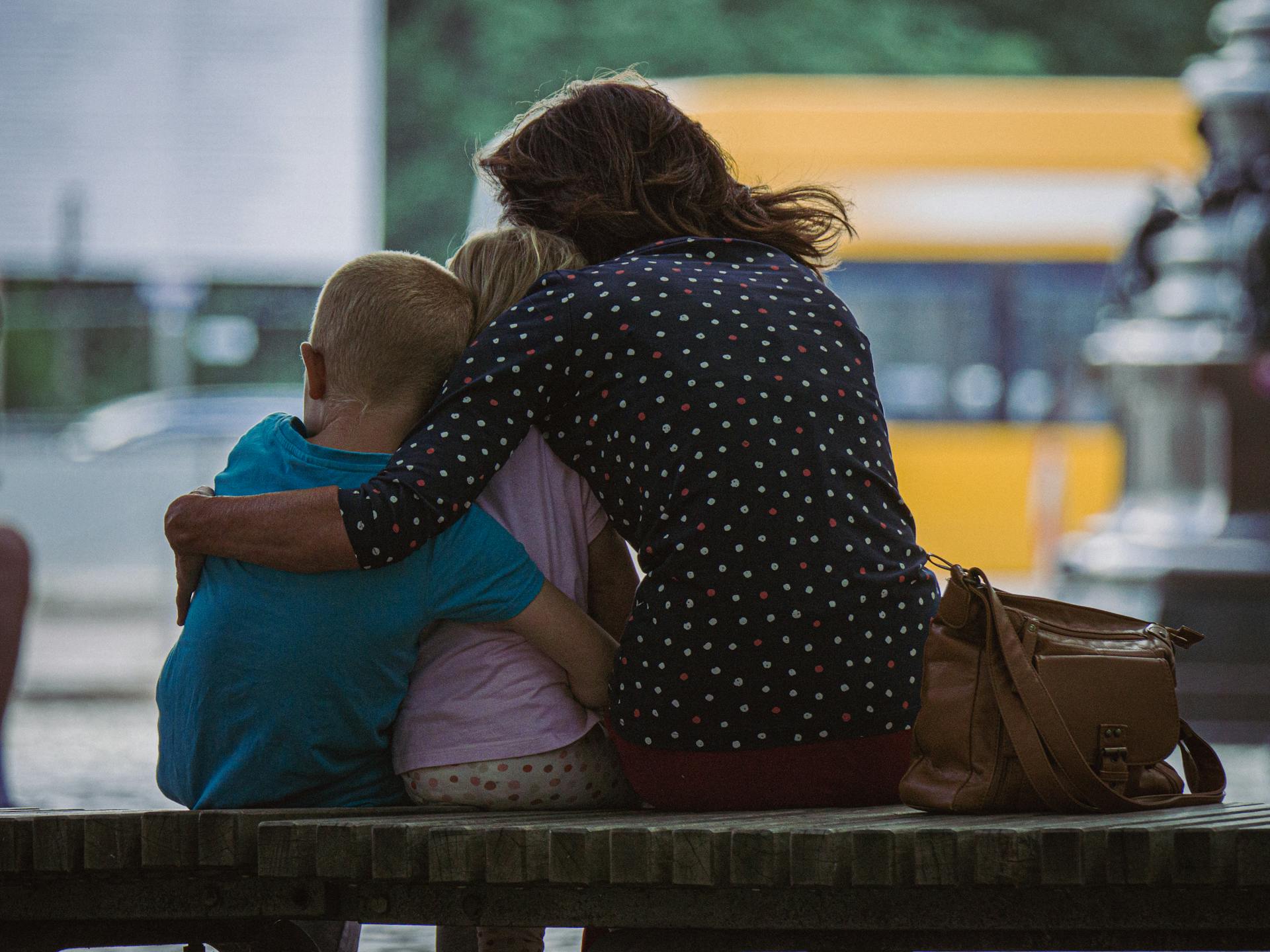 Vue de dos d'une femme serrant ses enfants dans ses bras alors qu'elle est assise sur un banc | Source : Pexels