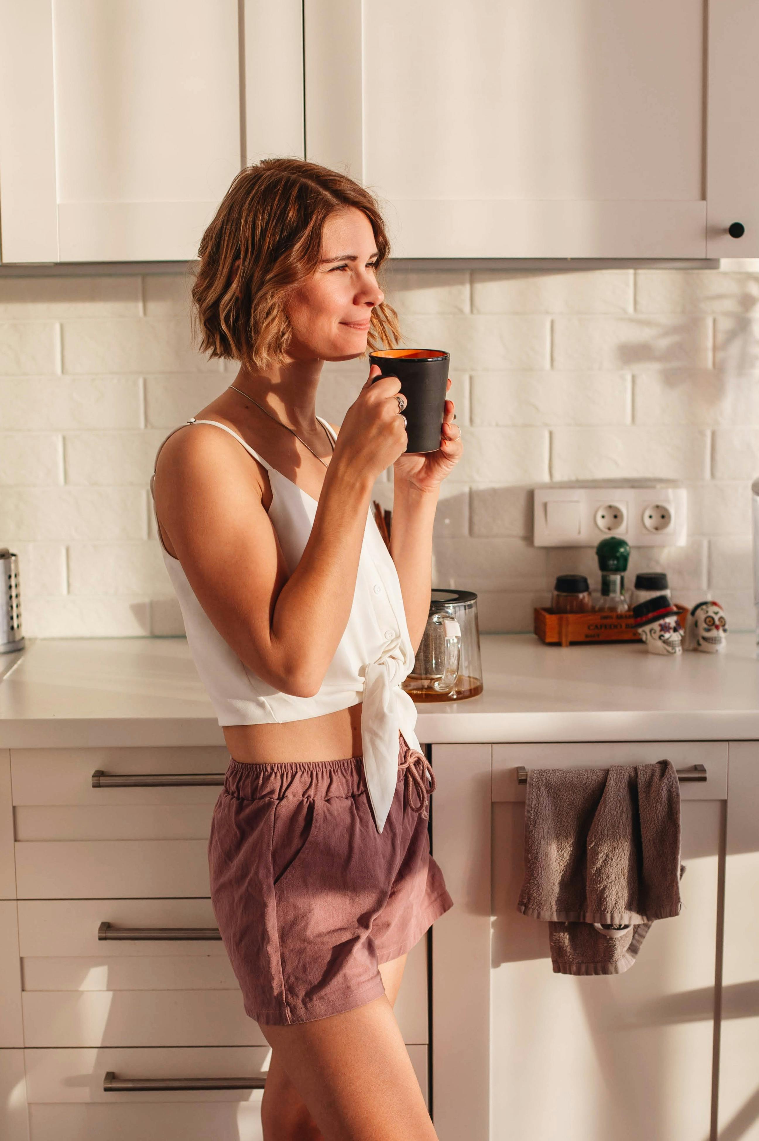 Une femme heureuse tenant une tasse de café dans la cuisine | Source : Pexels