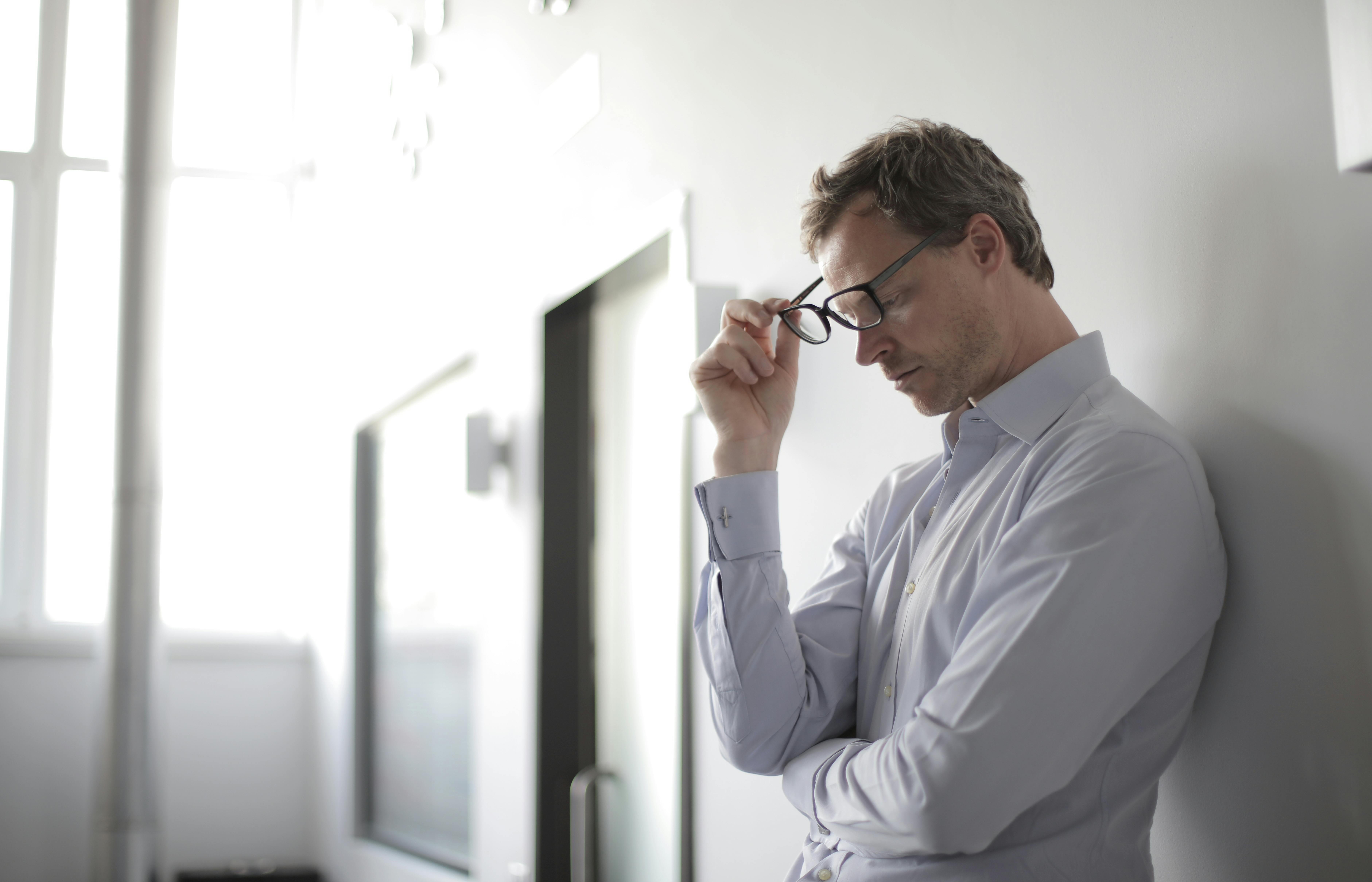 Un homme contrarié se tenant contre un mur avec ses lunettes partiellement enlevées | Source : Pexels