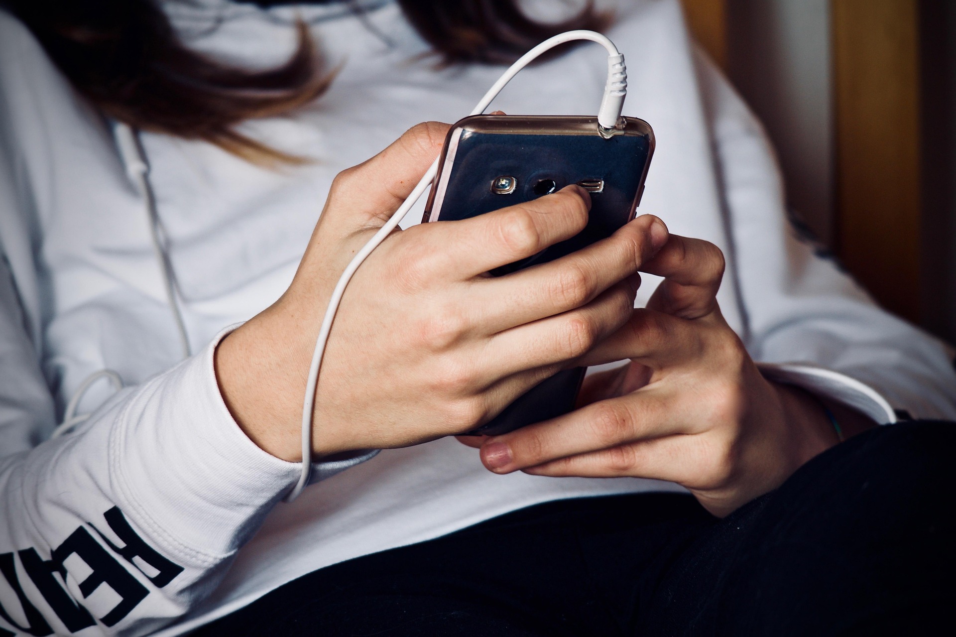 Une femme regardant un téléphone avec des écouteurs attachés | Source : Pixabay