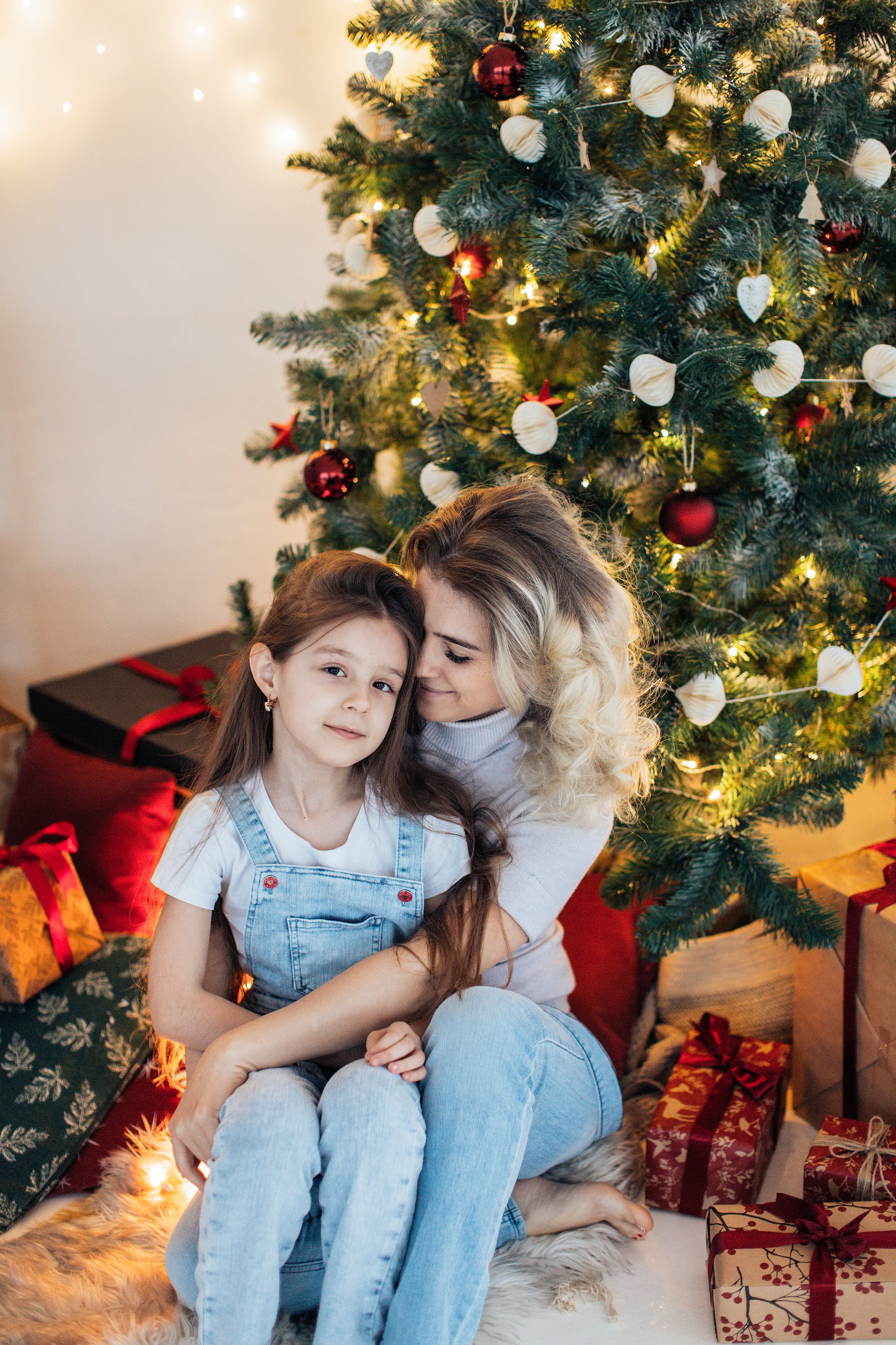 Une mère serrant sa fille dans ses bras alors qu'elle est assise à côté d'un sapin de Noël | Source : Pexels