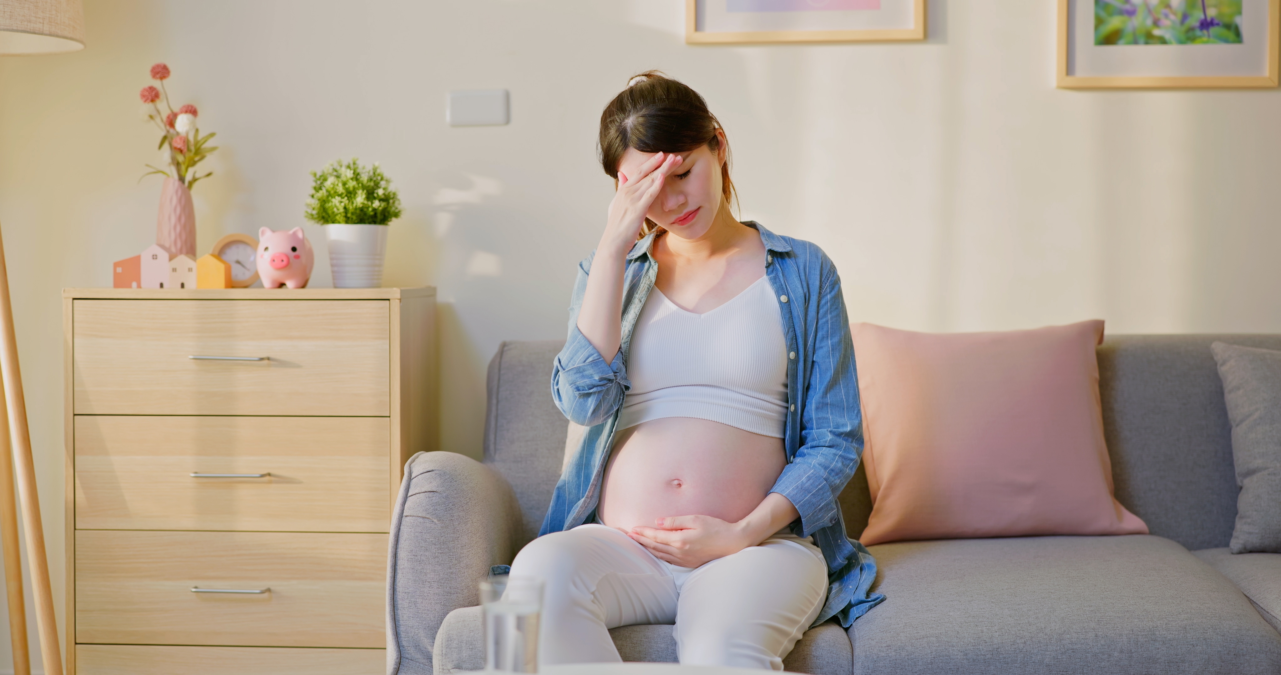 Une femme enceinte assise sur un canapé, la main sur le front | Source : Shutterstock