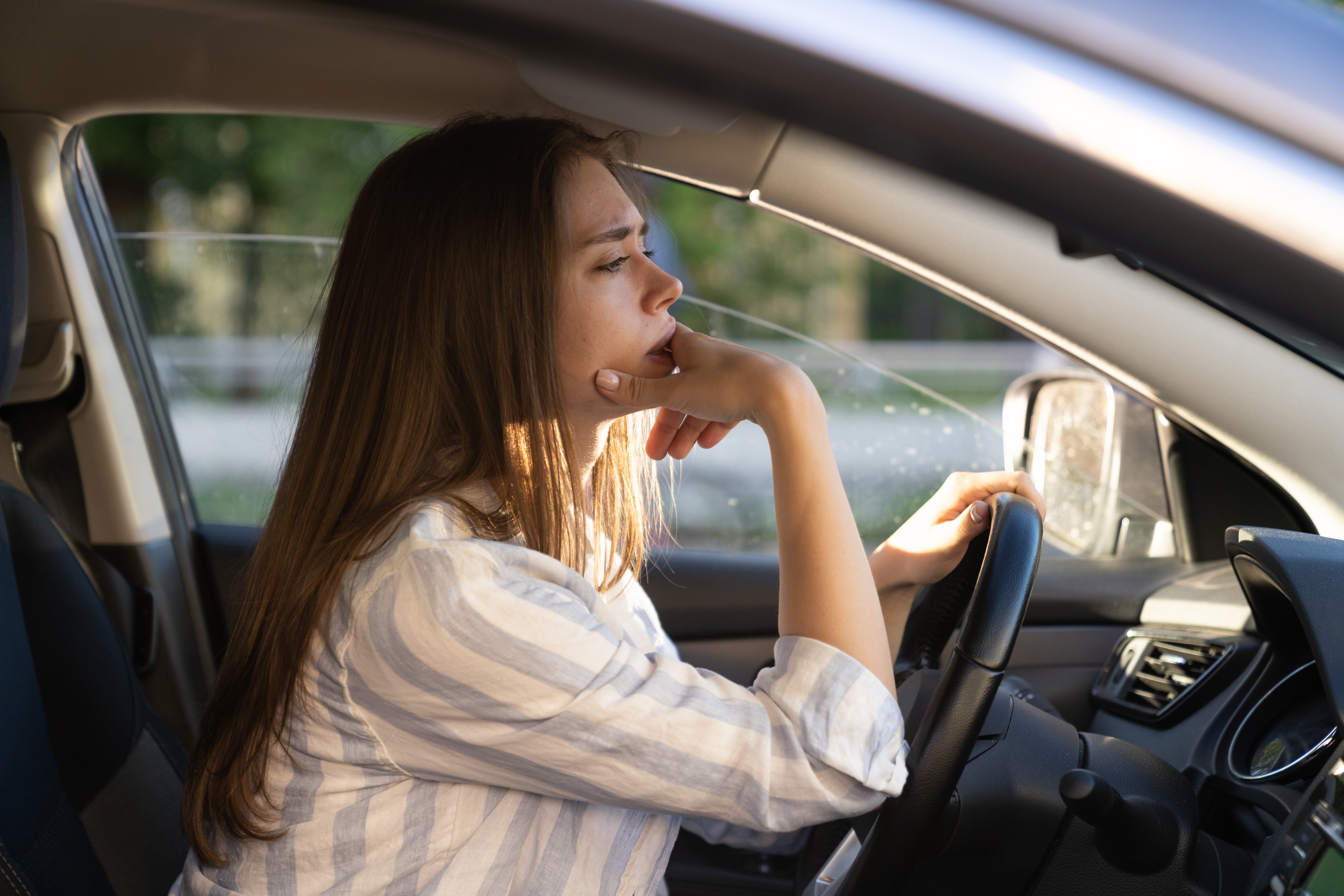 Une jeune femme triste et fatiguée au volant d'une voiture | Source : Shutterstock