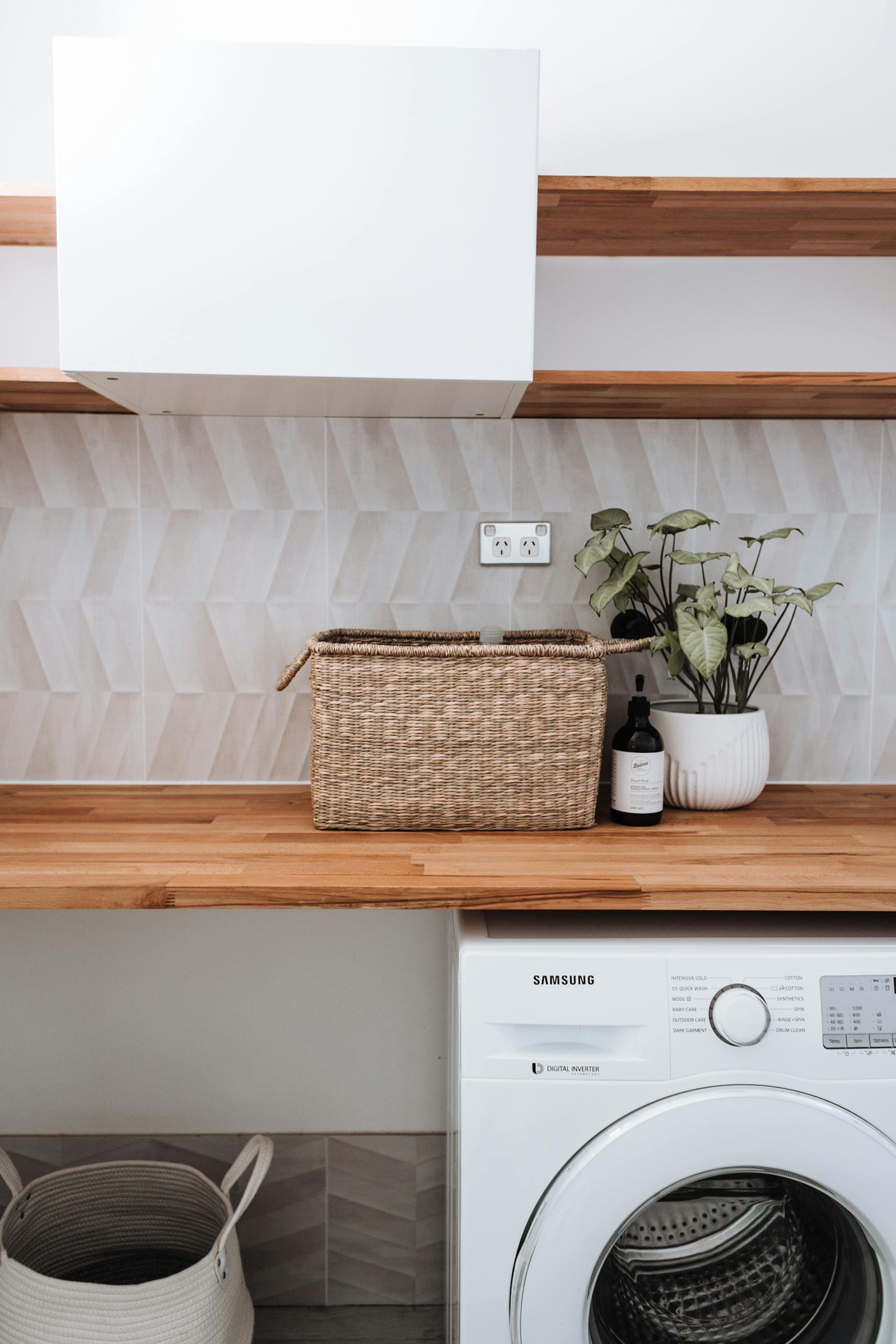 Une machine à laver sous une table en bois avec une plante et un panier en osier | Source : Pexels