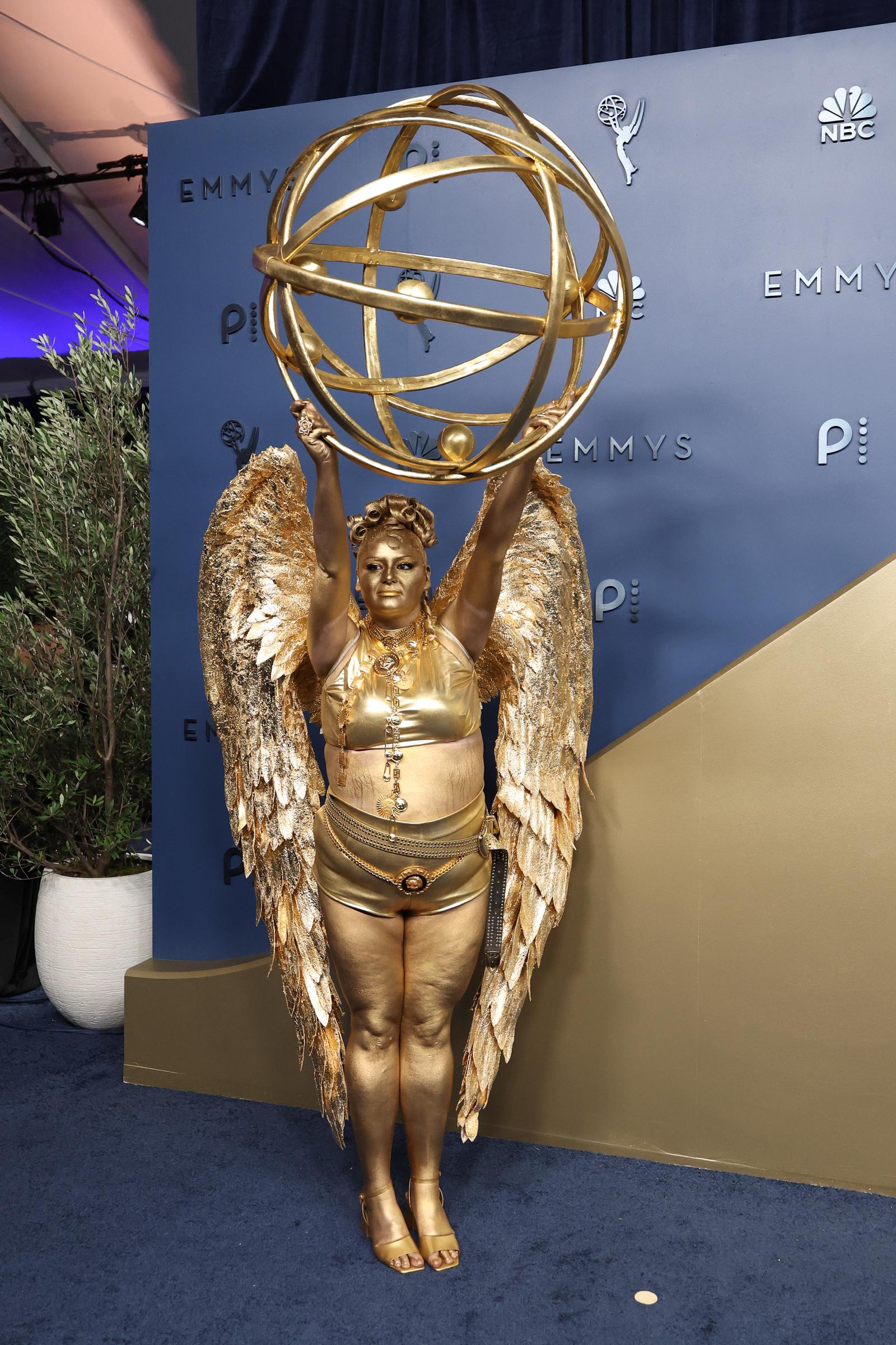 Meg Stalter pose dans une tenue entièrement dorée, avec des ailes spectaculaires et une statuette des Emmy surdimensionnée, lors de la 78e cérémonie des Primetime Emmy Awards. | Source : Getty Images