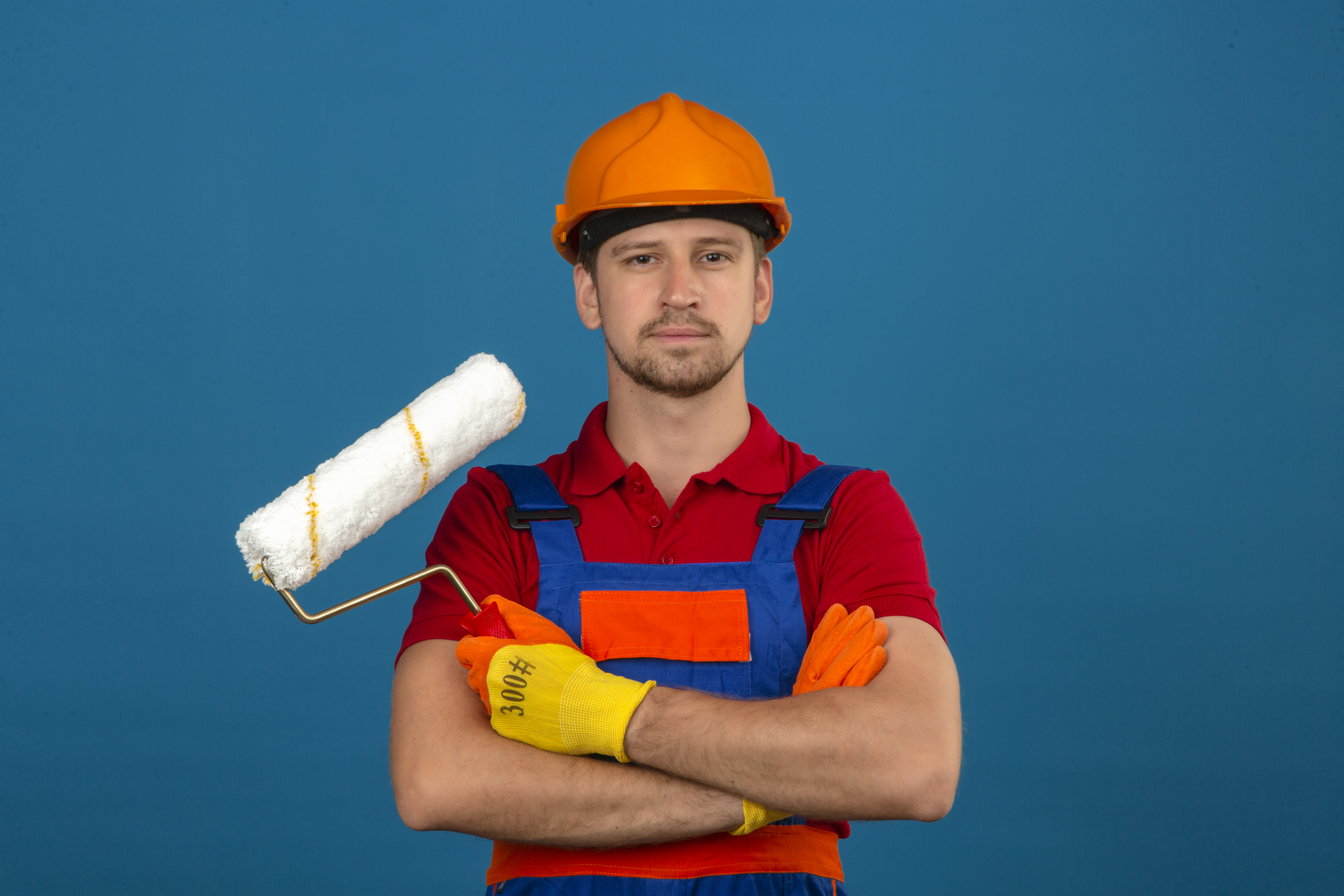 Un homme en uniforme de construction avec les bras croisés tout en tenant un rouleau | Source : Freepik