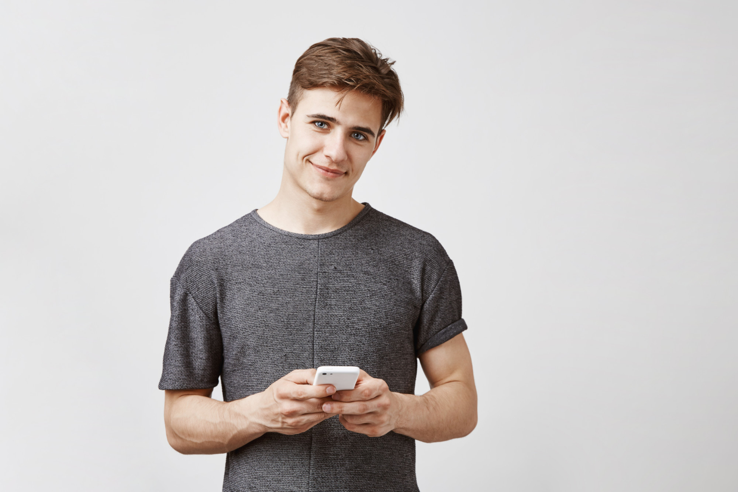 Un jeune homme souriant tenant son téléphone | Source : Freepik