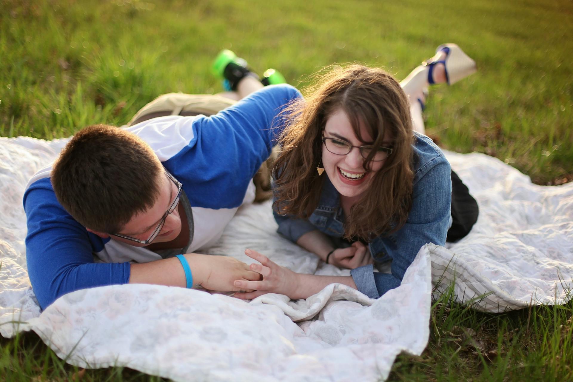 Un homme et une femme rient alors qu'ils sont allongés sur une natte dans l'herbe | Source : Pexels