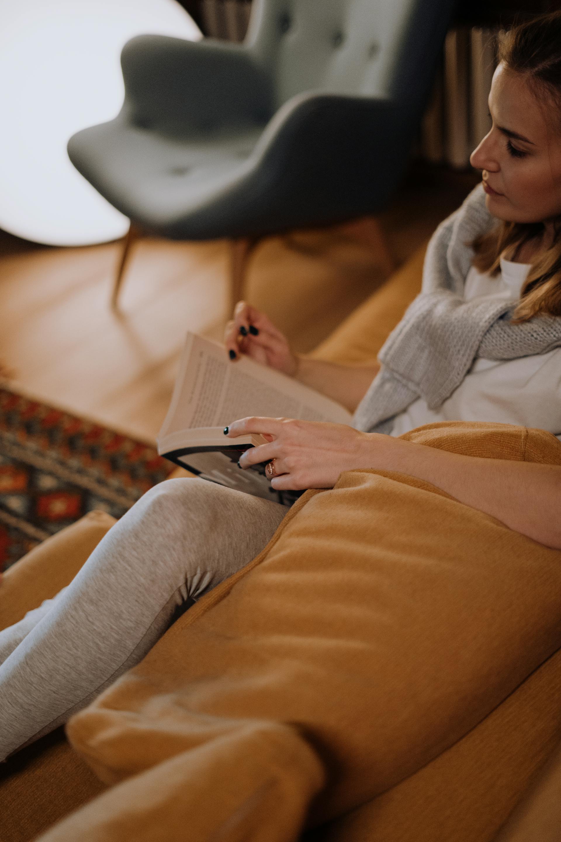 Une femme avec un livre sur le canapé | Source : Pexels