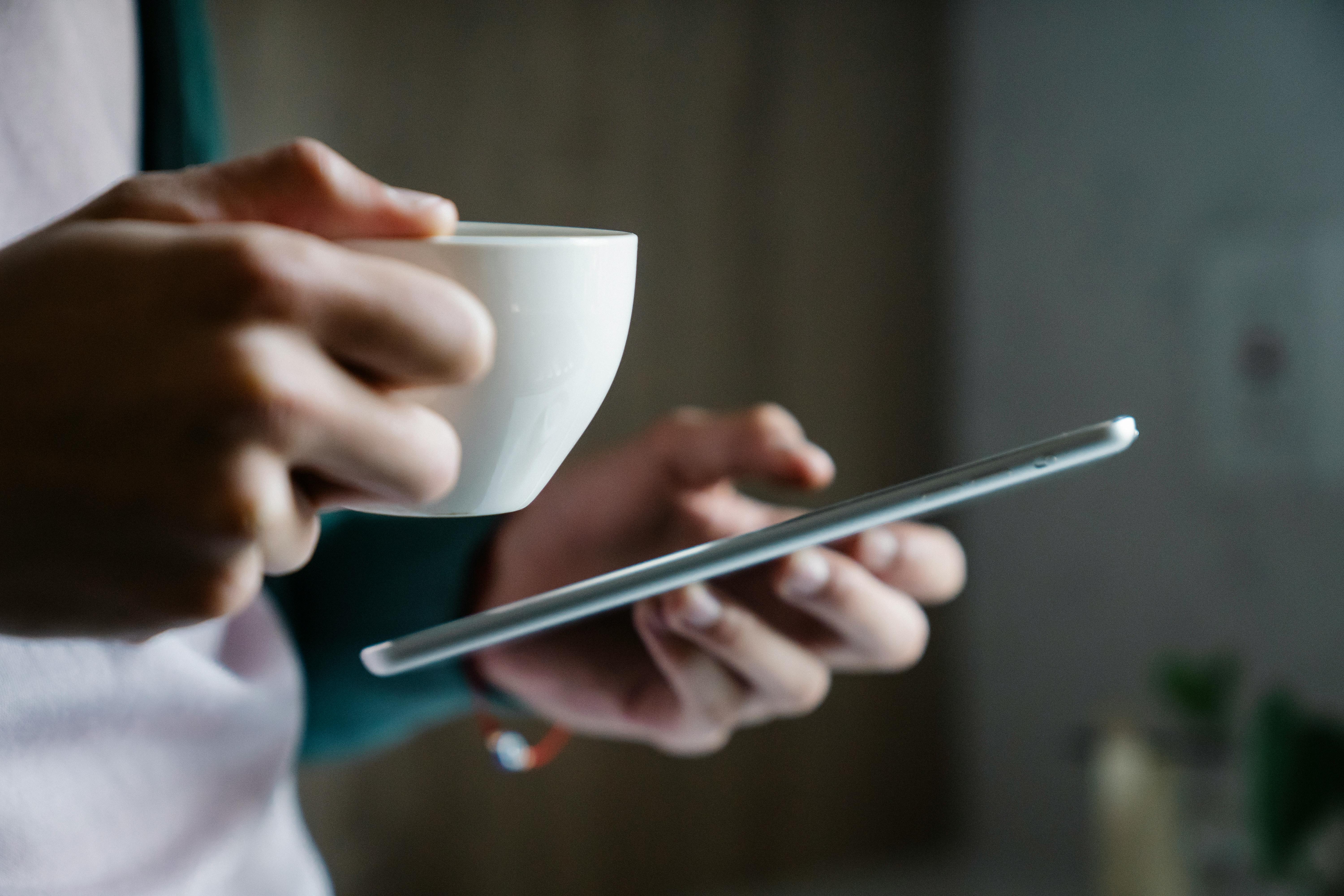 Gros plan sur une personne tenant une tasse de café et un smartphone | Source : Pexels