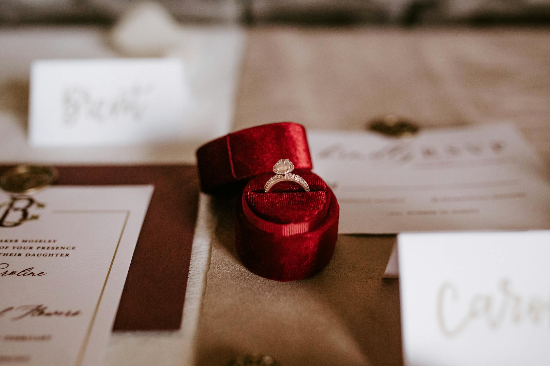 Une petite boîte rouge avec une bague posée sur une table avec des cartes d'invitation au mariage | Source : Pexels