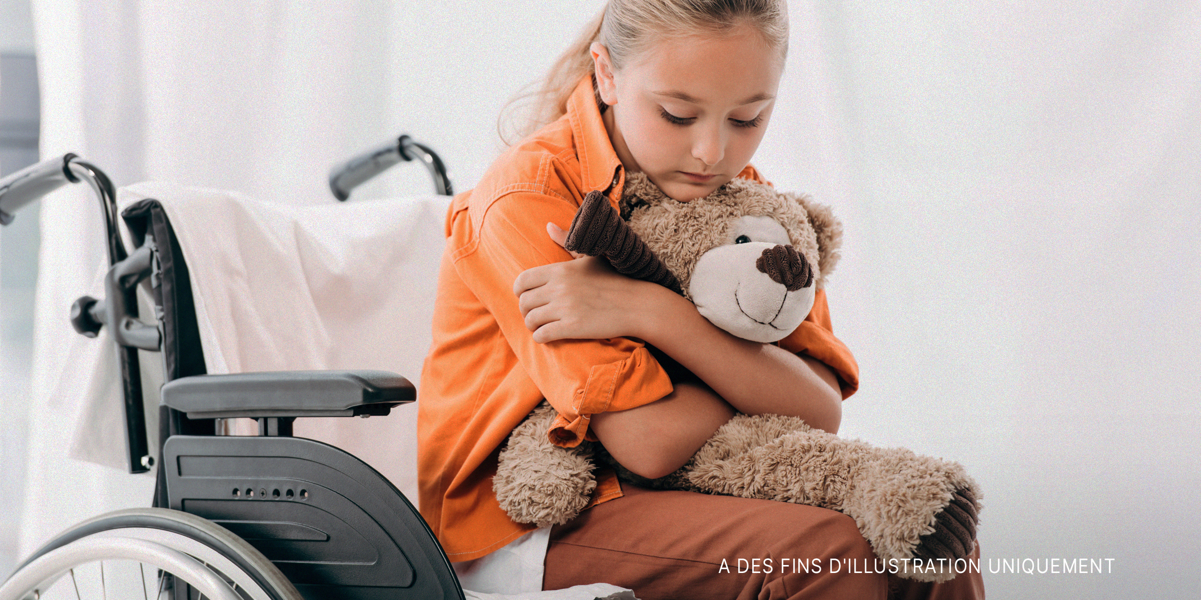 Enfant assise sur un fauteuil roulant avec un ours en peluche | Source : Shutterstock