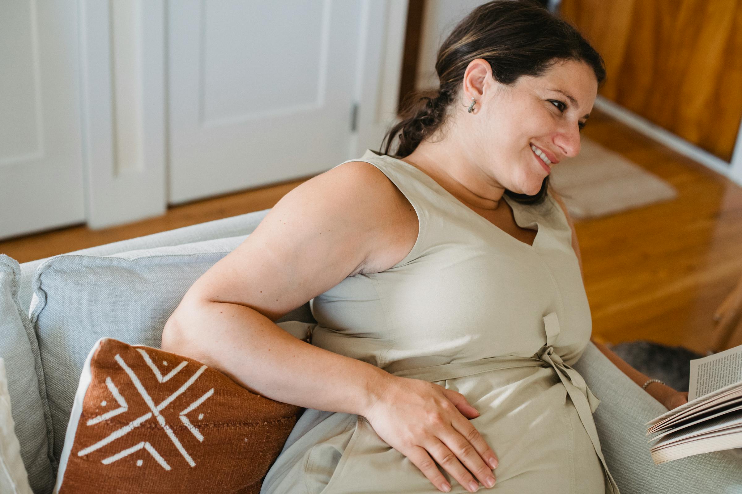 Une femme enceinte souriante et assise sur un canapé | Source : Pexels