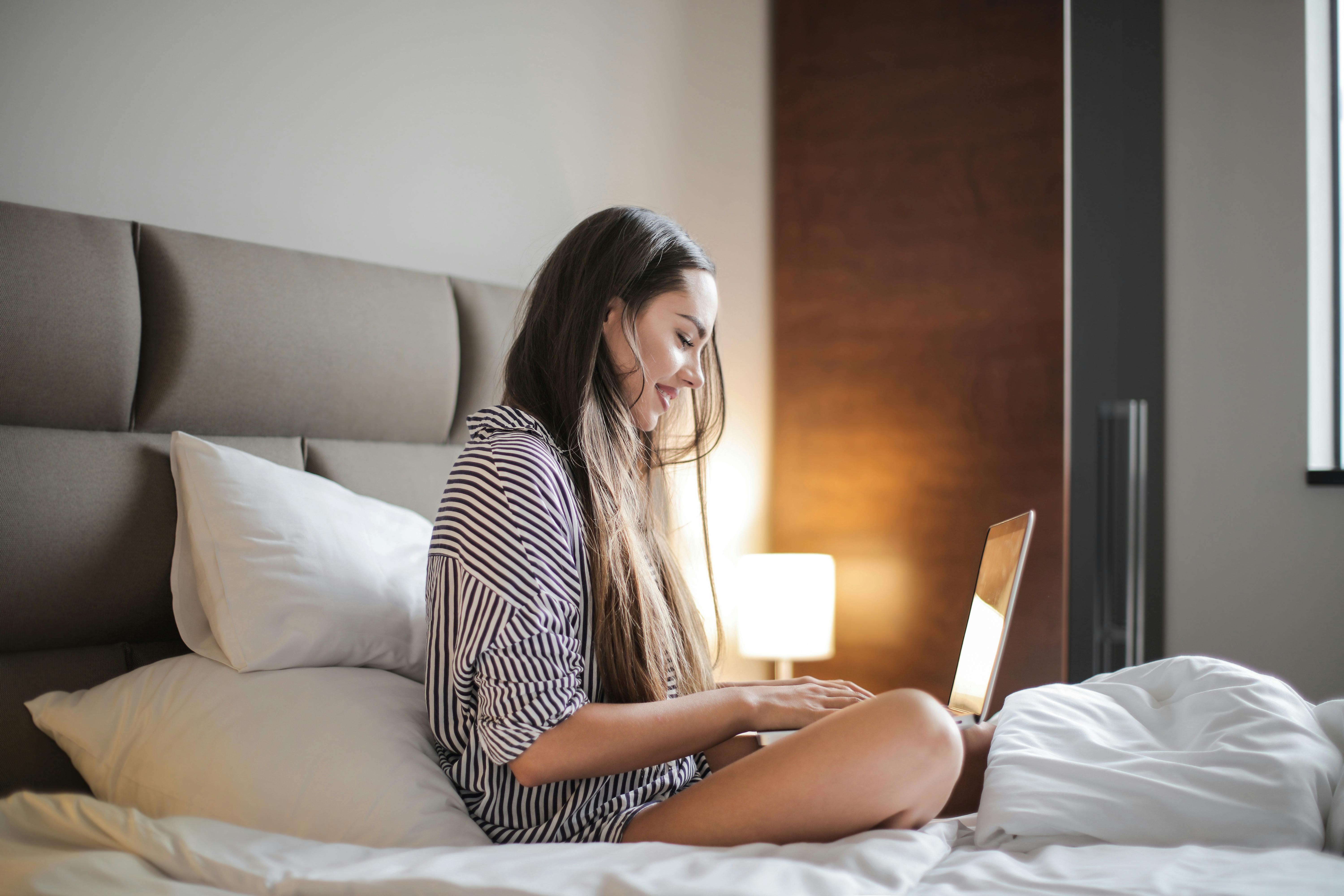 Une femme assise dans son lit et utilisant son ordinateur portable | Source : Pexels