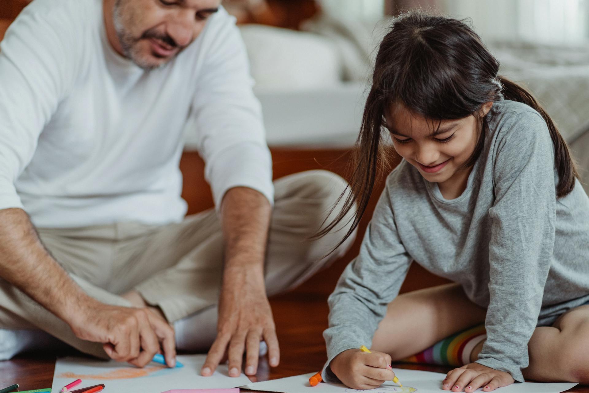 Un père et sa petite fille assis par terre et faisant du coloriage | Source : Pexels