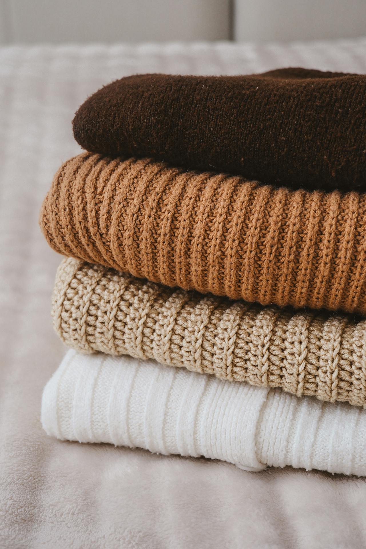 Une pile de pulls pliés sur le lit | Source : Pexels